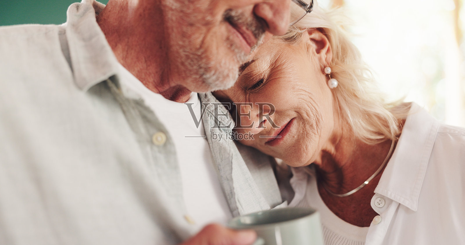 老年夫妇在家中拥抱，享受茶饮，幸福的妻子在厨房里感受爱与亲密。老年人微笑相拥，支持健康的婚姻，咖啡杯和退休承诺。照片摄影图片