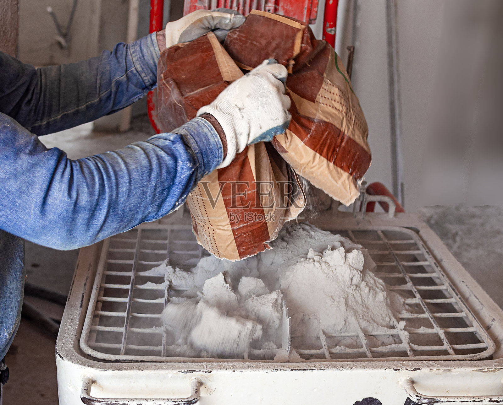 工人将一袋干石膏倒入混合槽，以便将干石膏与水混合并自动喂入成品石膏。照片摄影图片