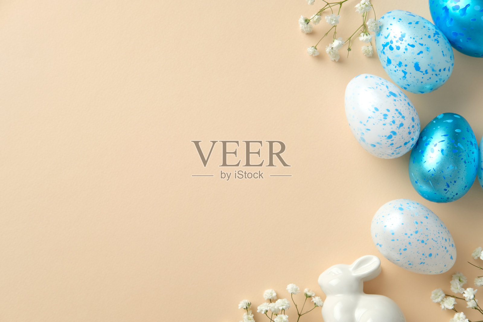 复活节快乐贺卡模板。蓝白相间的斑点蛋、陶瓷兔子和细小的花朵，背景为柔和的米色。照片摄影图片