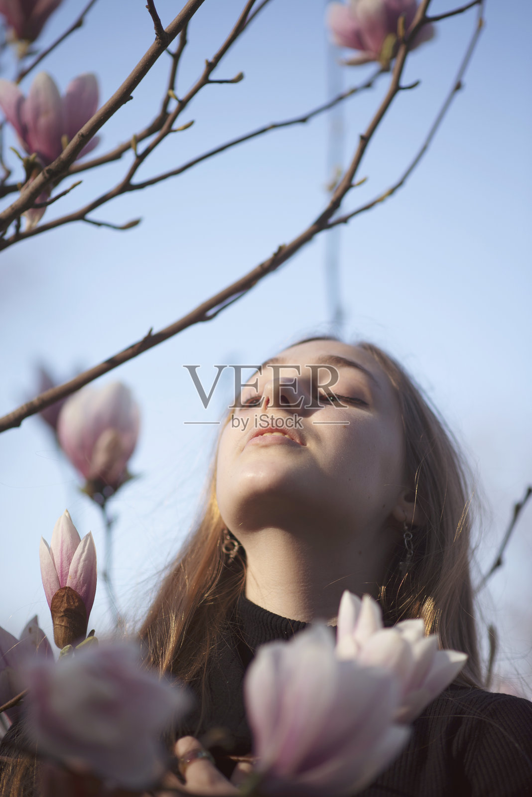 年轻的金发女孩与盛开的粉色玉兰树。一个女人站在树旁。照片摄影图片