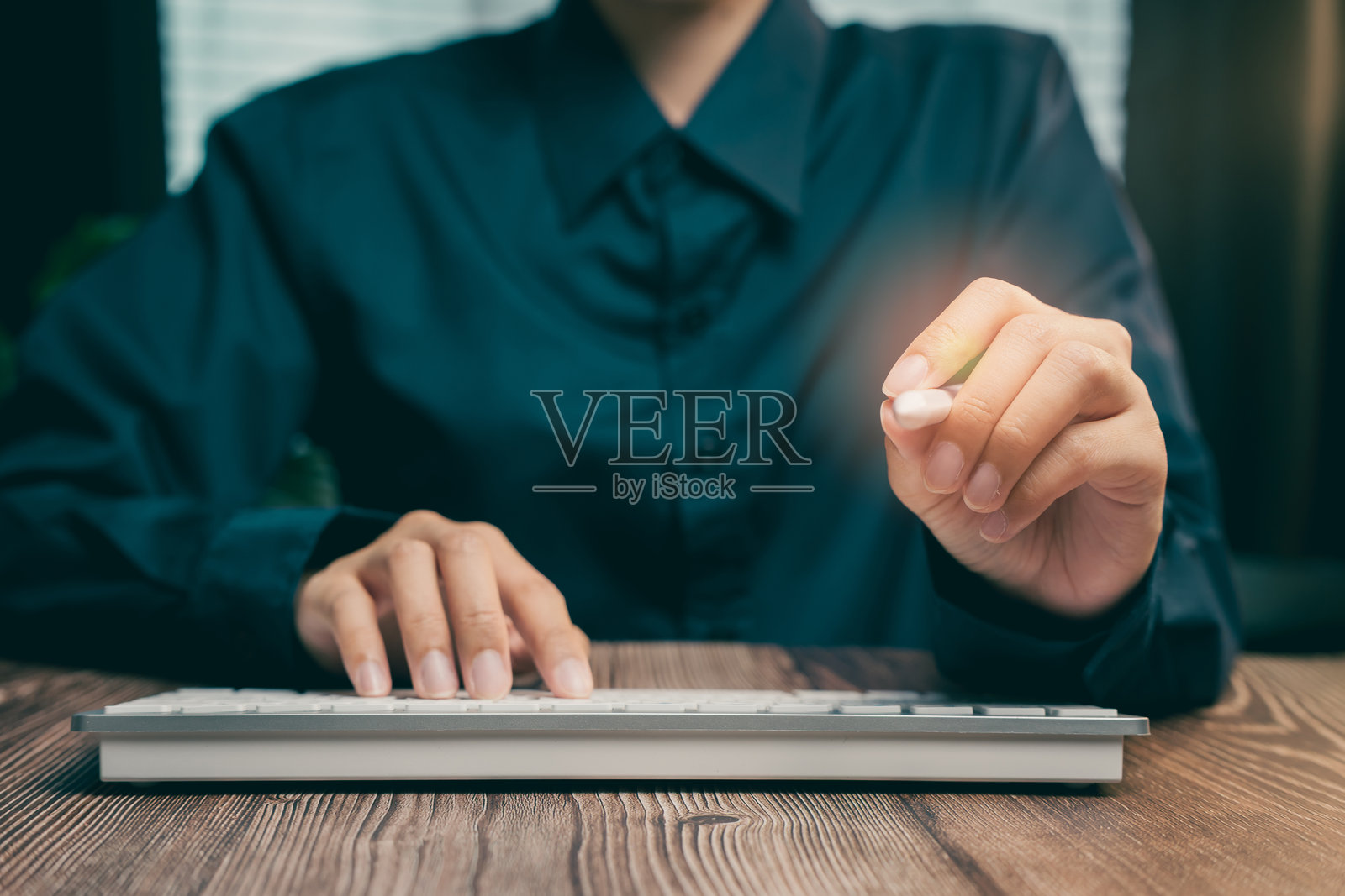 在现代工作环境中，专业人士一边打字一边握着笔，商业概念照片摄影图片