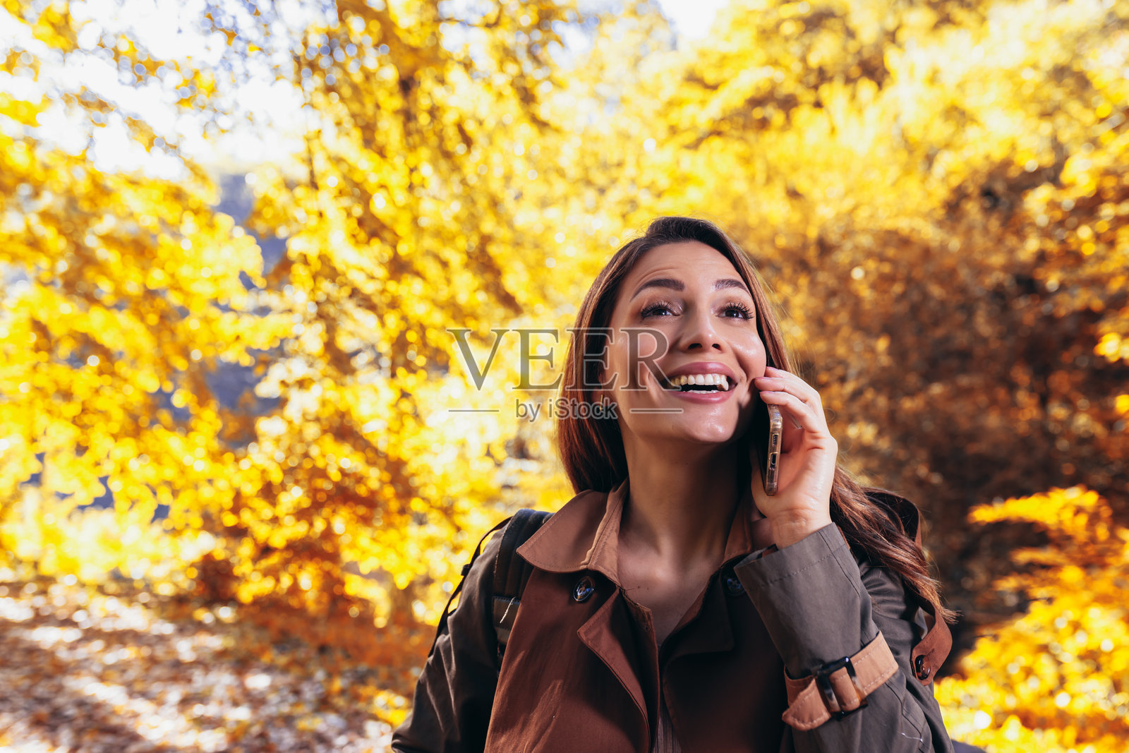 快乐的年轻女性在秋天的公园里使用手机。照片摄影图片