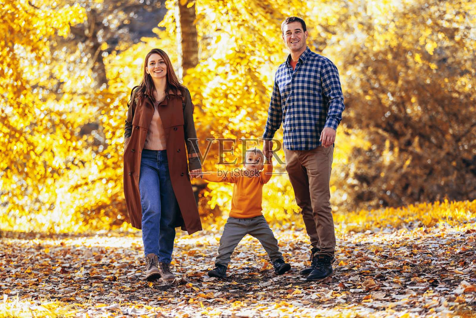 幸福的一家三口在美丽的秋季公园散步。照片摄影图片