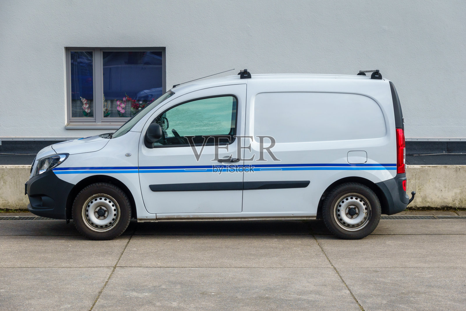 住宅区的紧凑型面包车 - 一辆带蓝色条纹的白色面包车停在房屋墙前。照片摄影图片