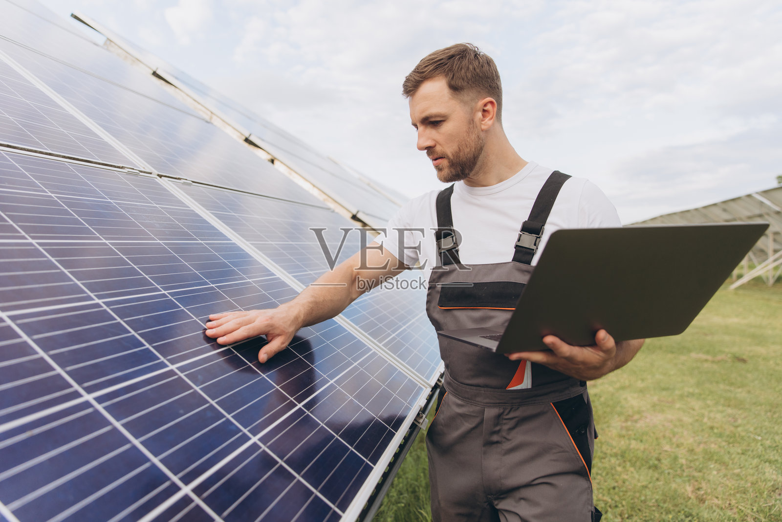 工程师或建筑工人，留着胡子的男人使用笔记本电脑检查太阳能电池板系统状态。电池电厂。增强现实概念。未来科技。照片摄影图片