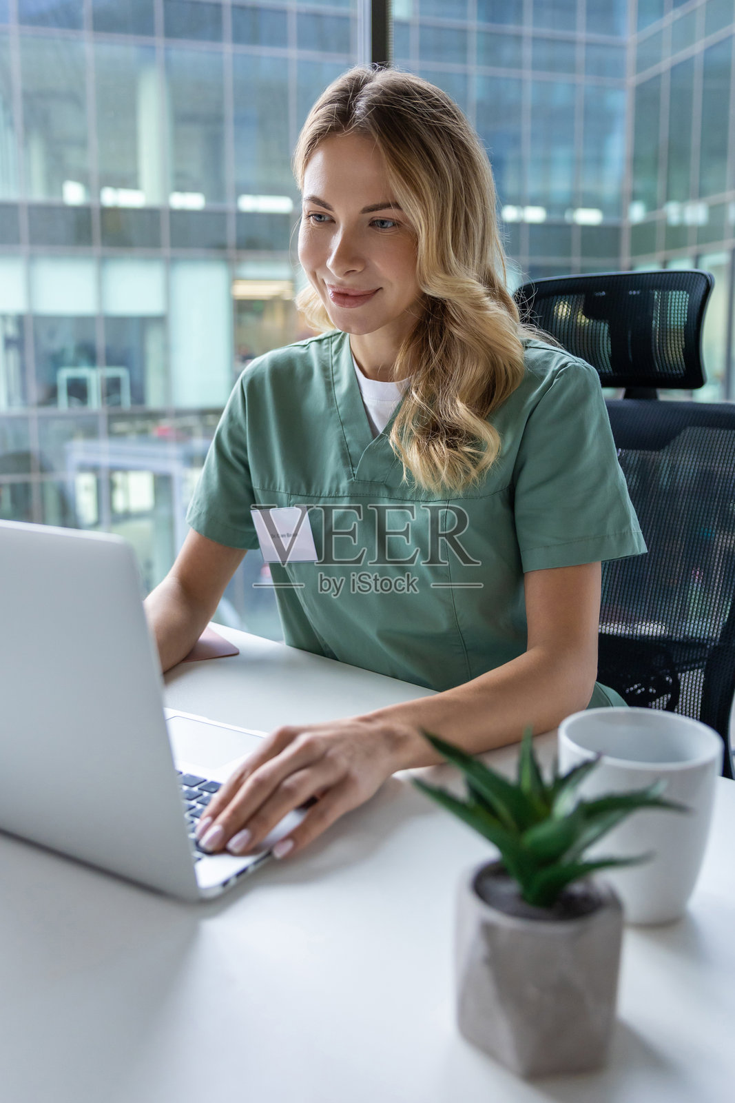 女医生坐在医院的工作桌前，使用笔记本电脑。照片摄影图片