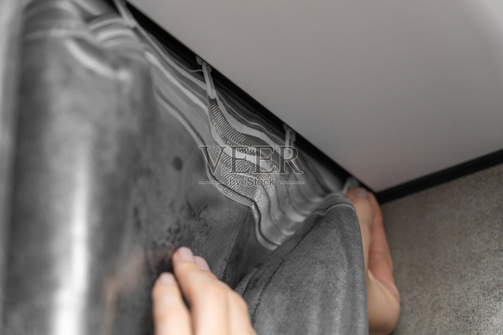 特写镜头展示双手在天花板轨道上安装灰色条纹窗帘，突显现代时尚居住空间中家居装饰的精致过程。照片摄影图片
