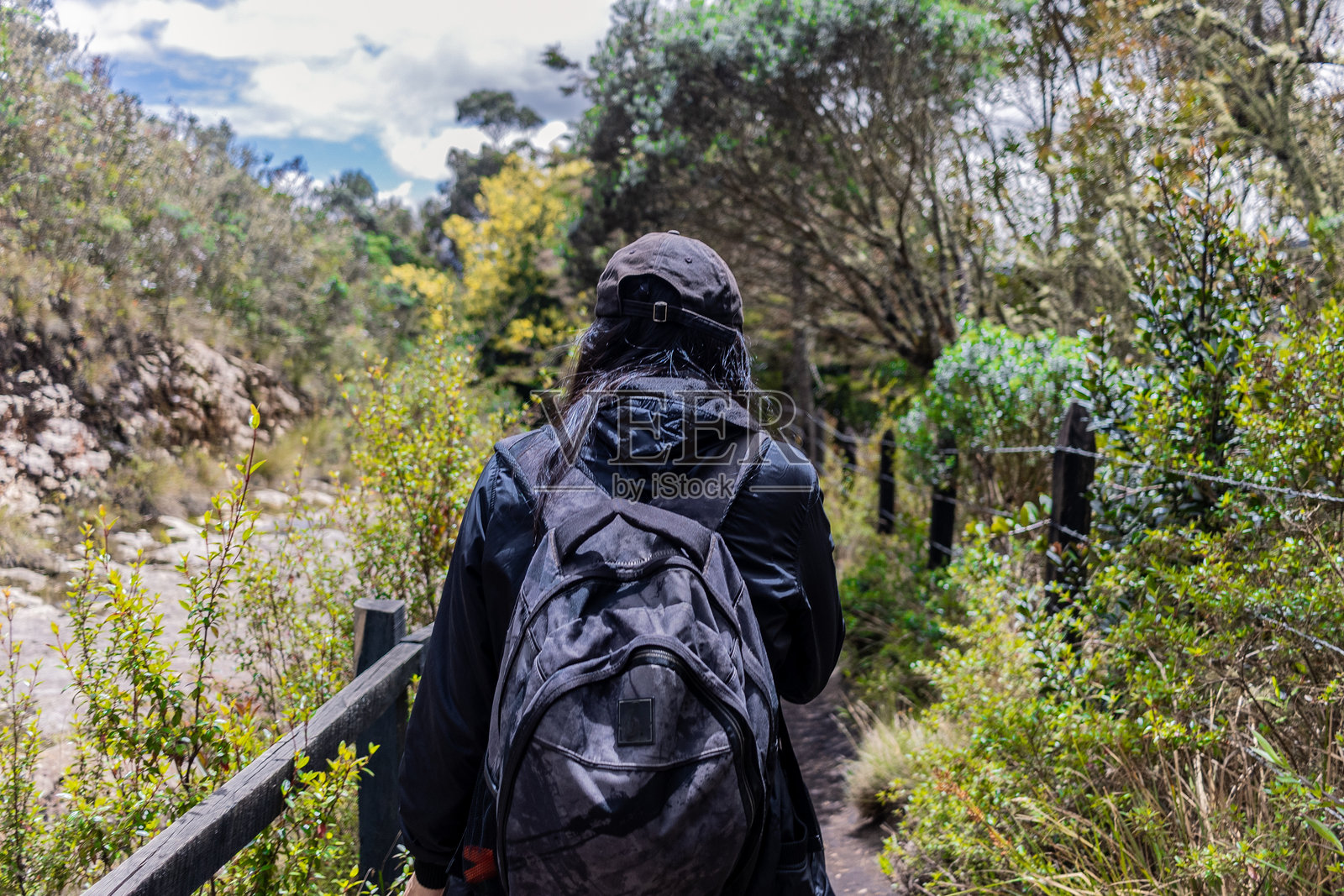 年轻女性旅行者戴着帽子，背着旅行箱，在山间小径上徒步旅行照片摄影图片