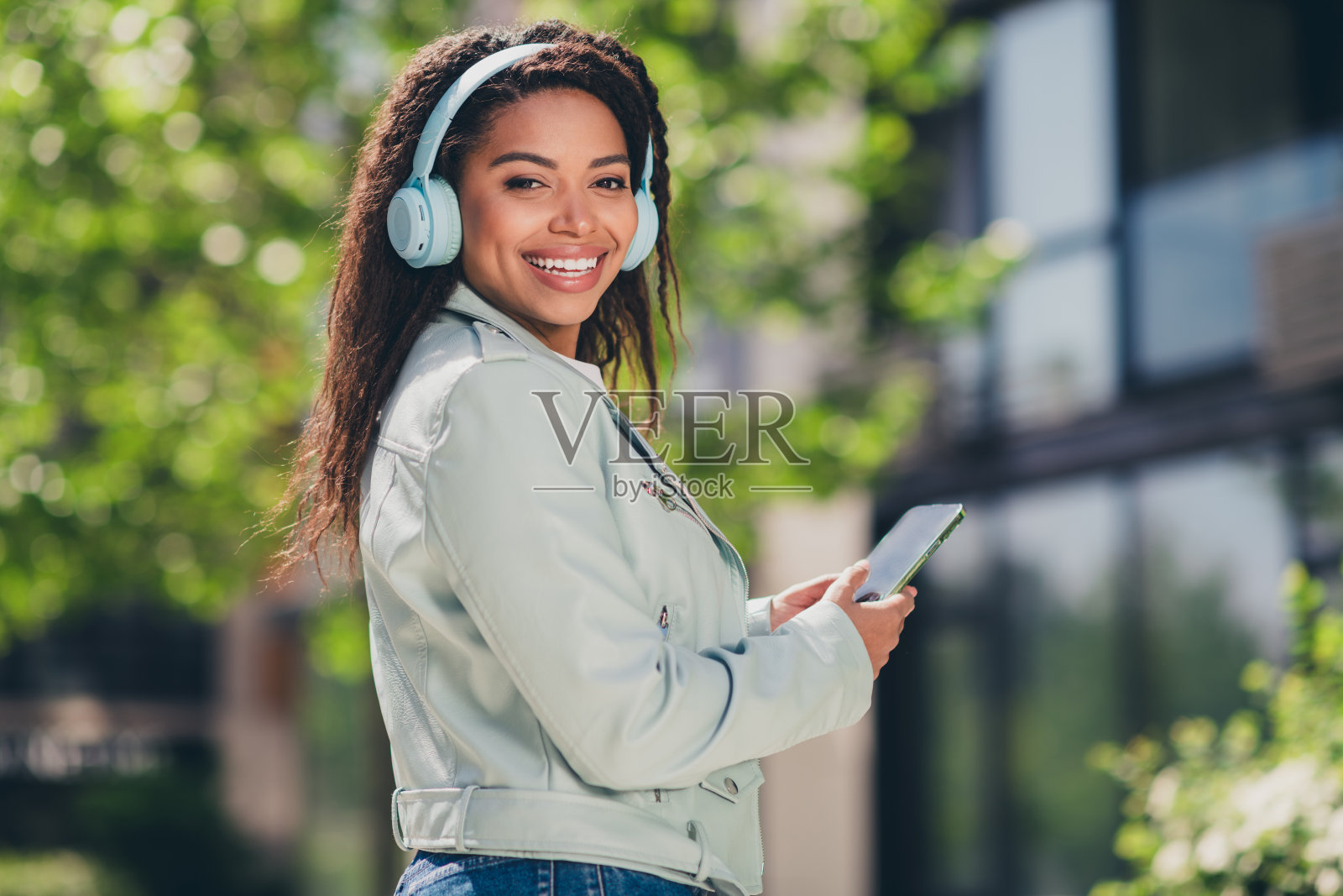 年轻女性在城市环境中享受阳光，戴着耳机，手持智能手机照片摄影图片