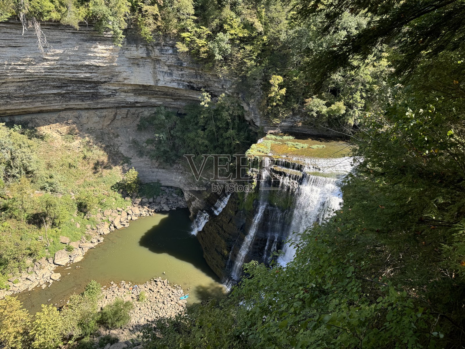 壮观的瀑布倾泻入宁静的水池，四周环绕着郁郁葱葱的绿植，阳光明媚。照片摄影图片