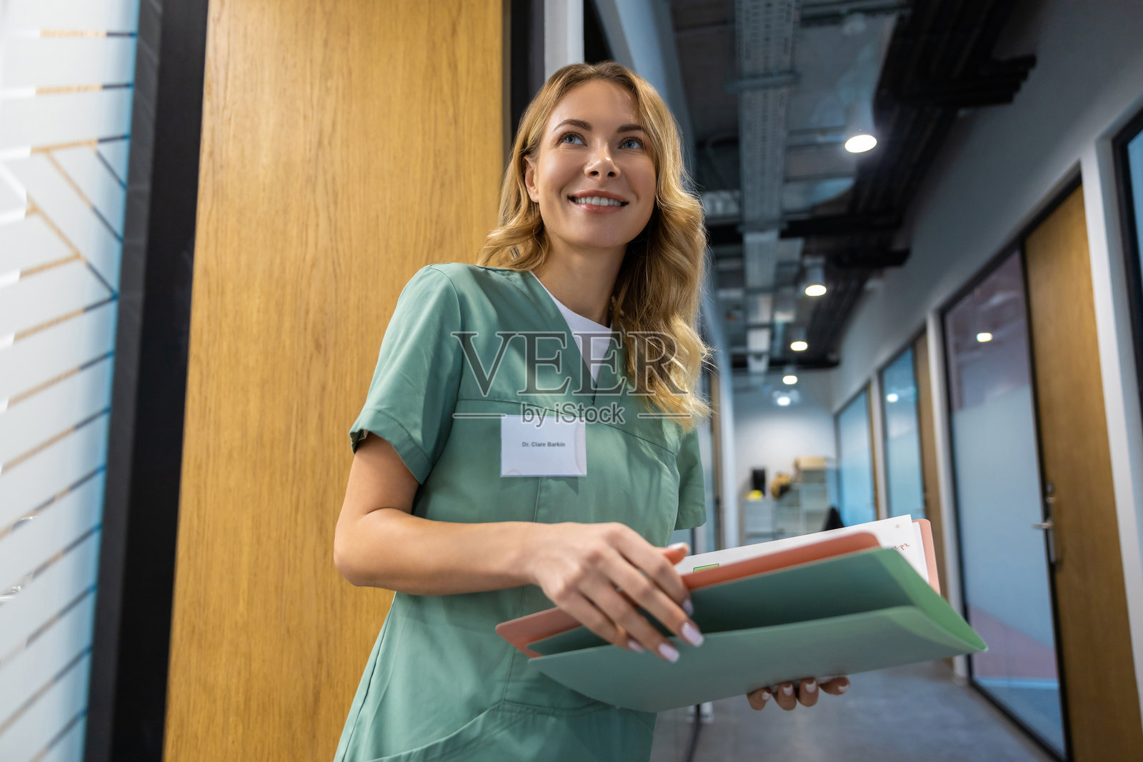 女医生站在医院走廊，手里拿着病例和医疗文件。照片摄影图片