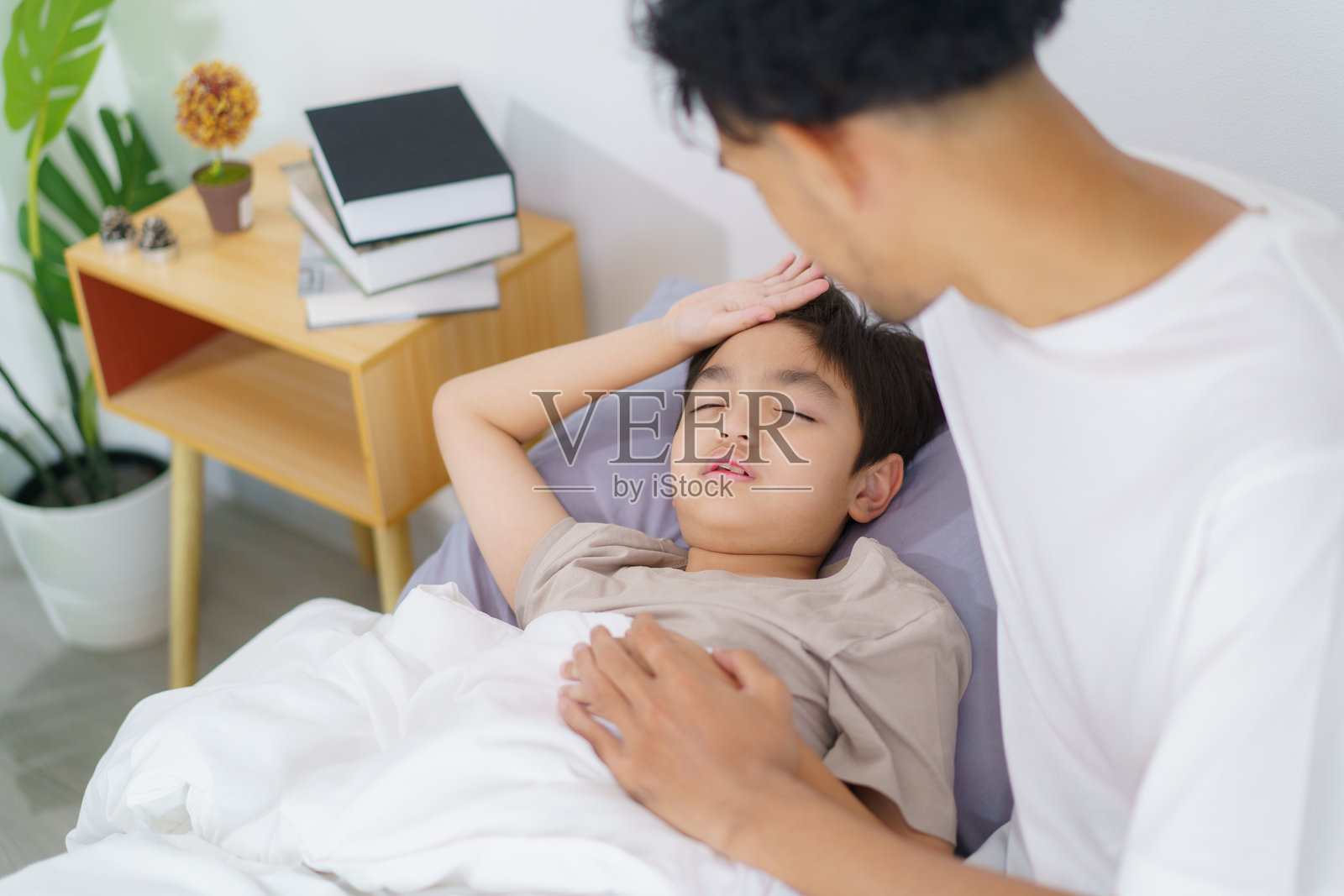 一位亚洲男子正在照顾他正在床上睡觉或休息的儿子。照片摄影图片