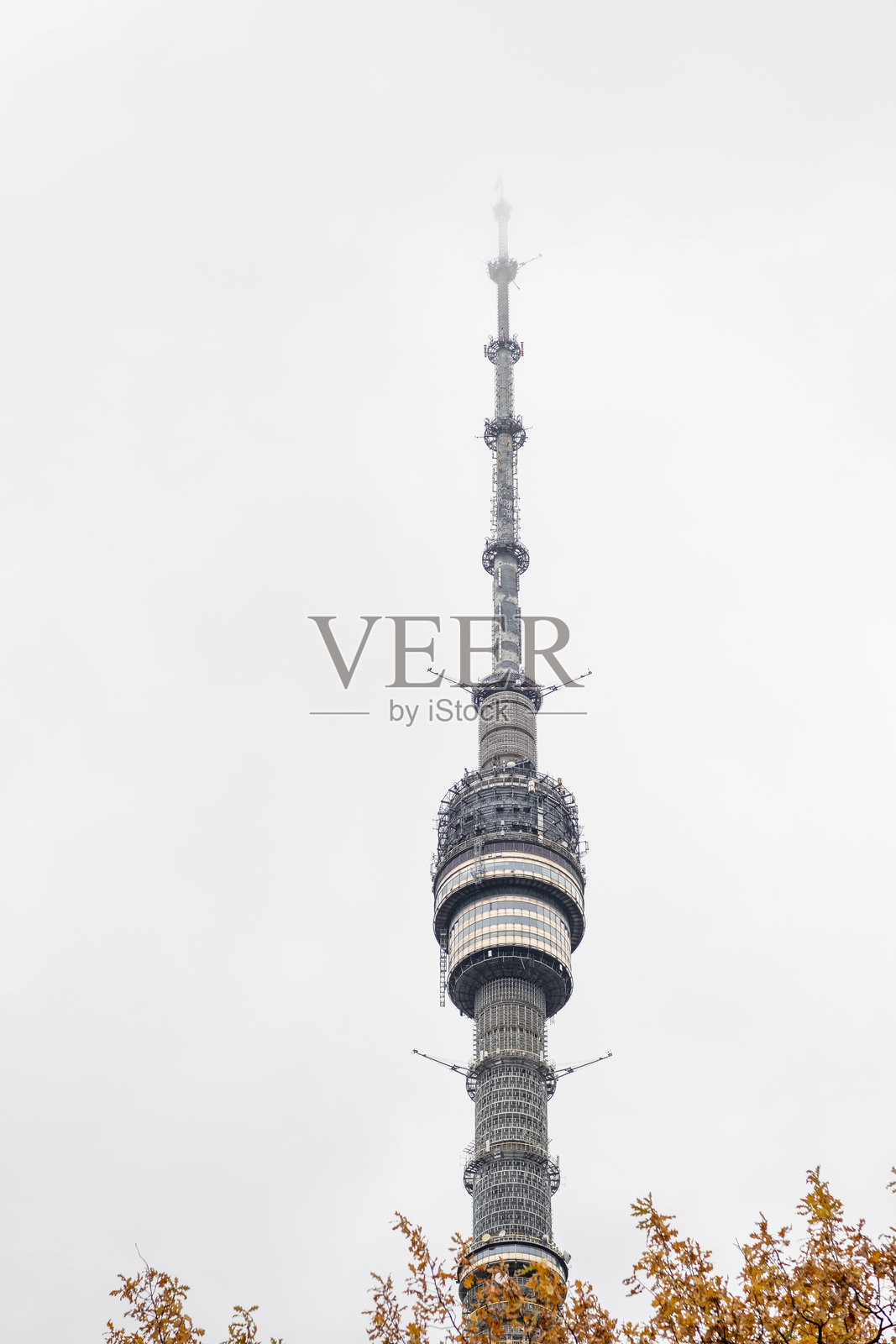 现代通信塔被秋天的树叶环绕，城市中阴云密布的日子。照片摄影图片