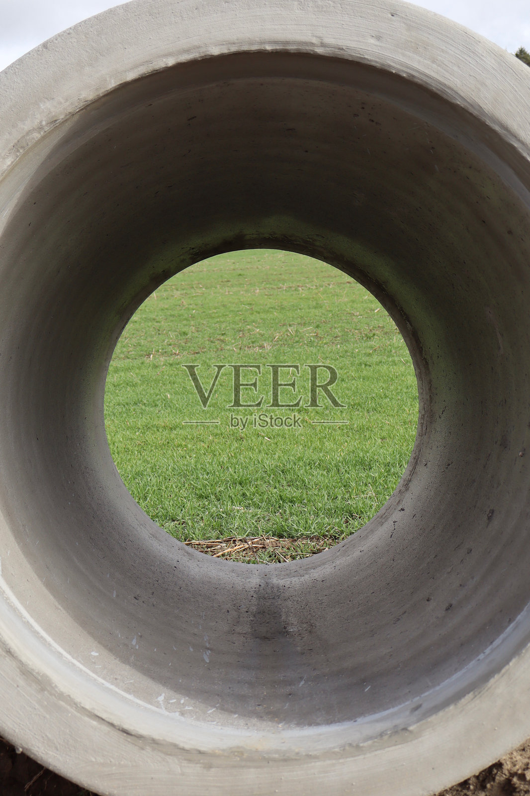 一个圆形开口的混凝土管道框住了一片绿色的田野。照片摄影图片