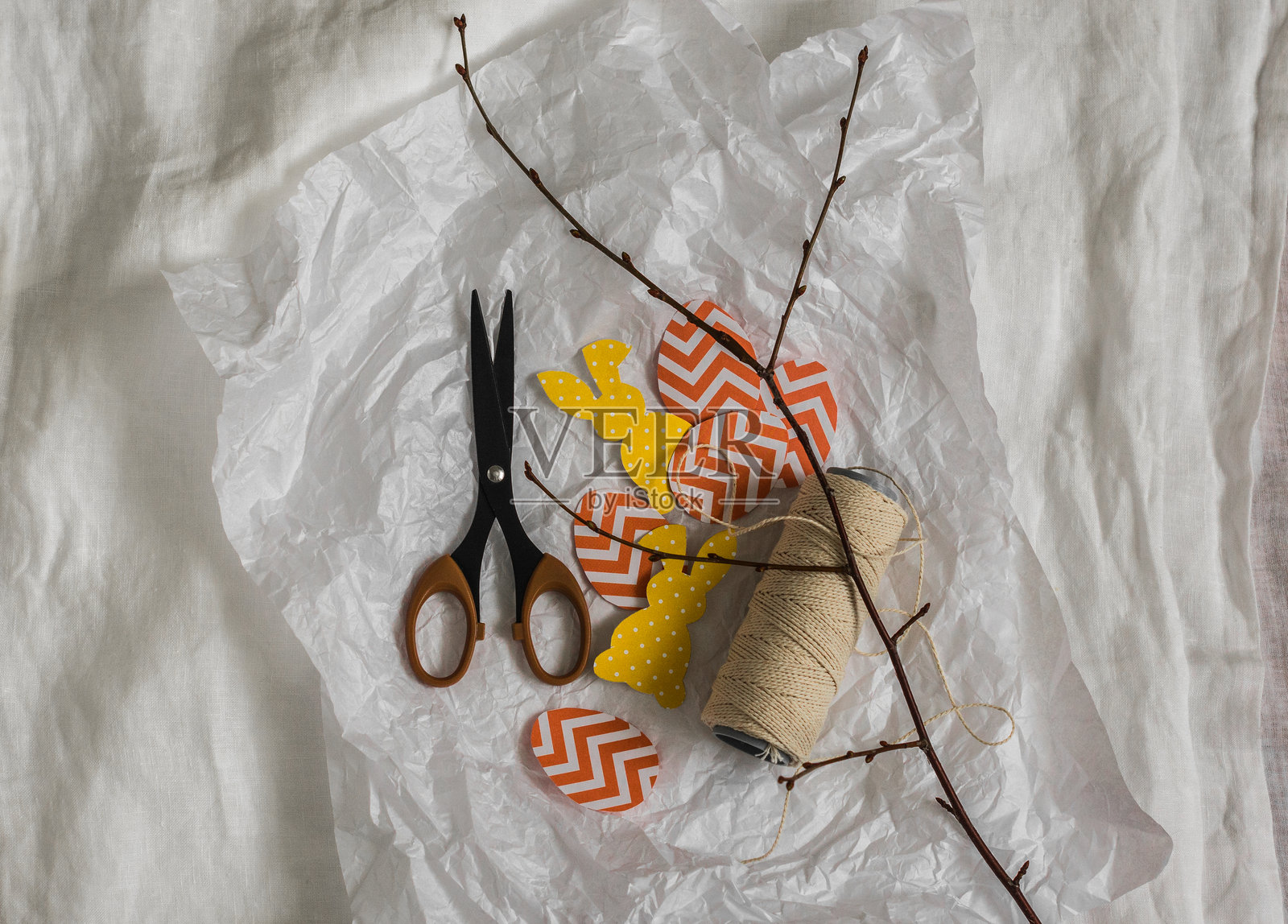 制作复活节花环的细节 - 纸兔子、彩蛋、剪刀、麻绳在浅色背景上，俯视图照片摄影图片