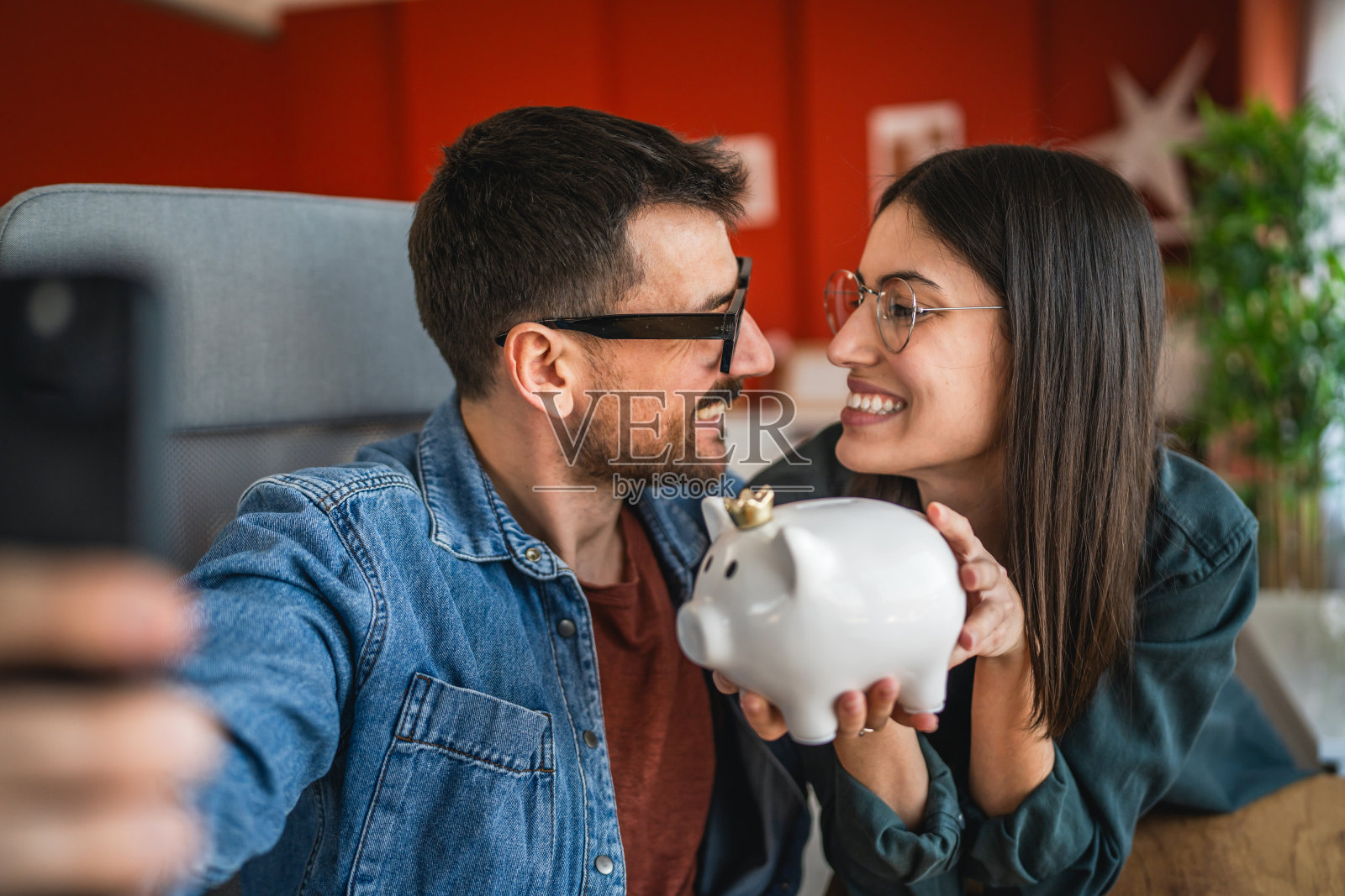 一对情侣在家中自拍或视频通话，同时手里拿着储蓄罐。照片摄影图片