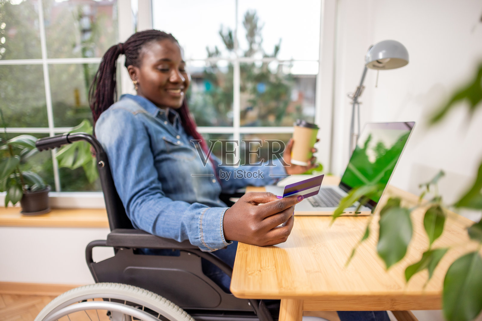 微笑的女性坐在轮椅上，使用笔记本电脑和信用卡在线管理财务照片摄影图片