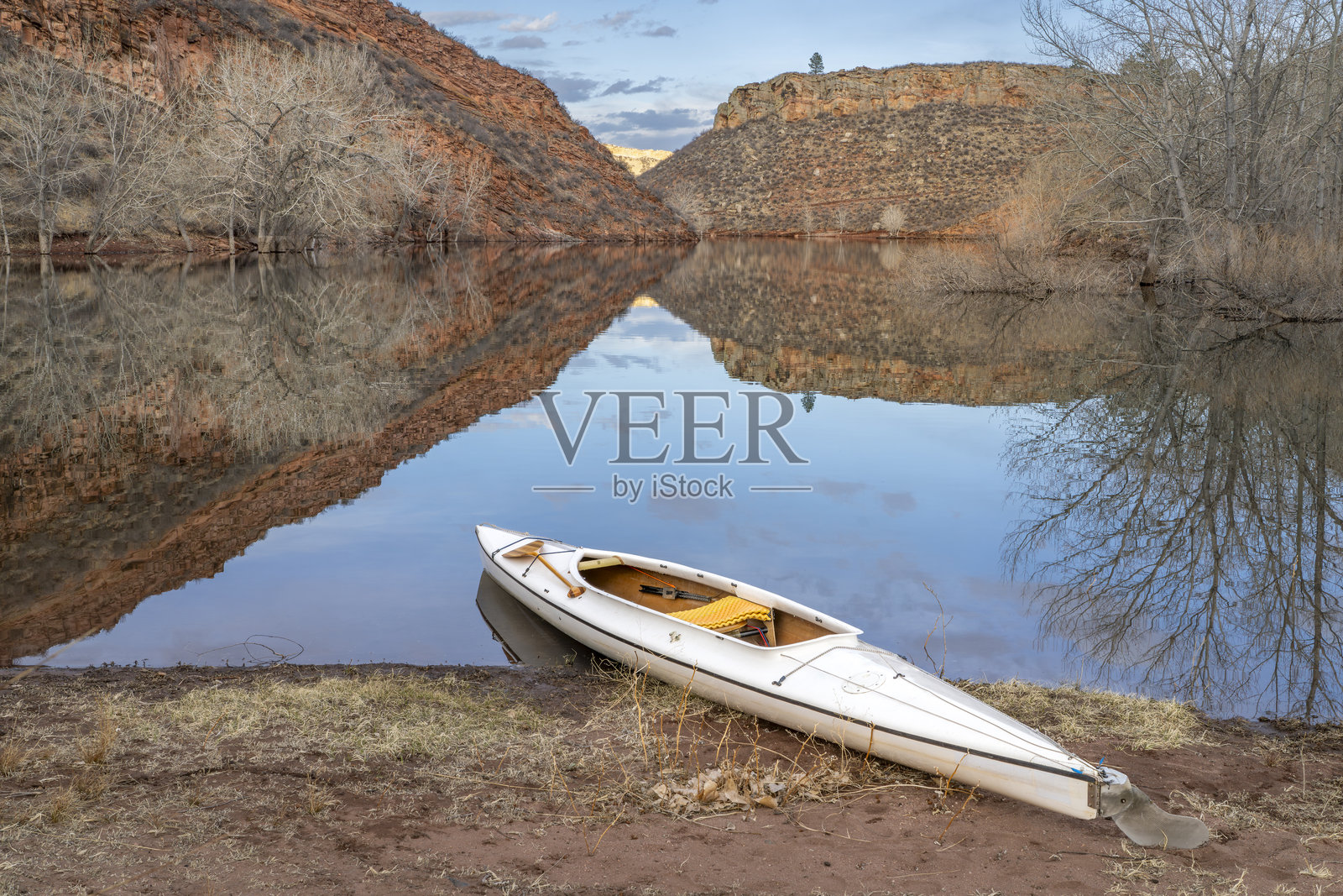 装饰精美的探险独木舟，配有木桨，停靠在科罗拉多州北部霍斯图斯水库的岸边，背景是寒冷季节的风景。照片摄影图片