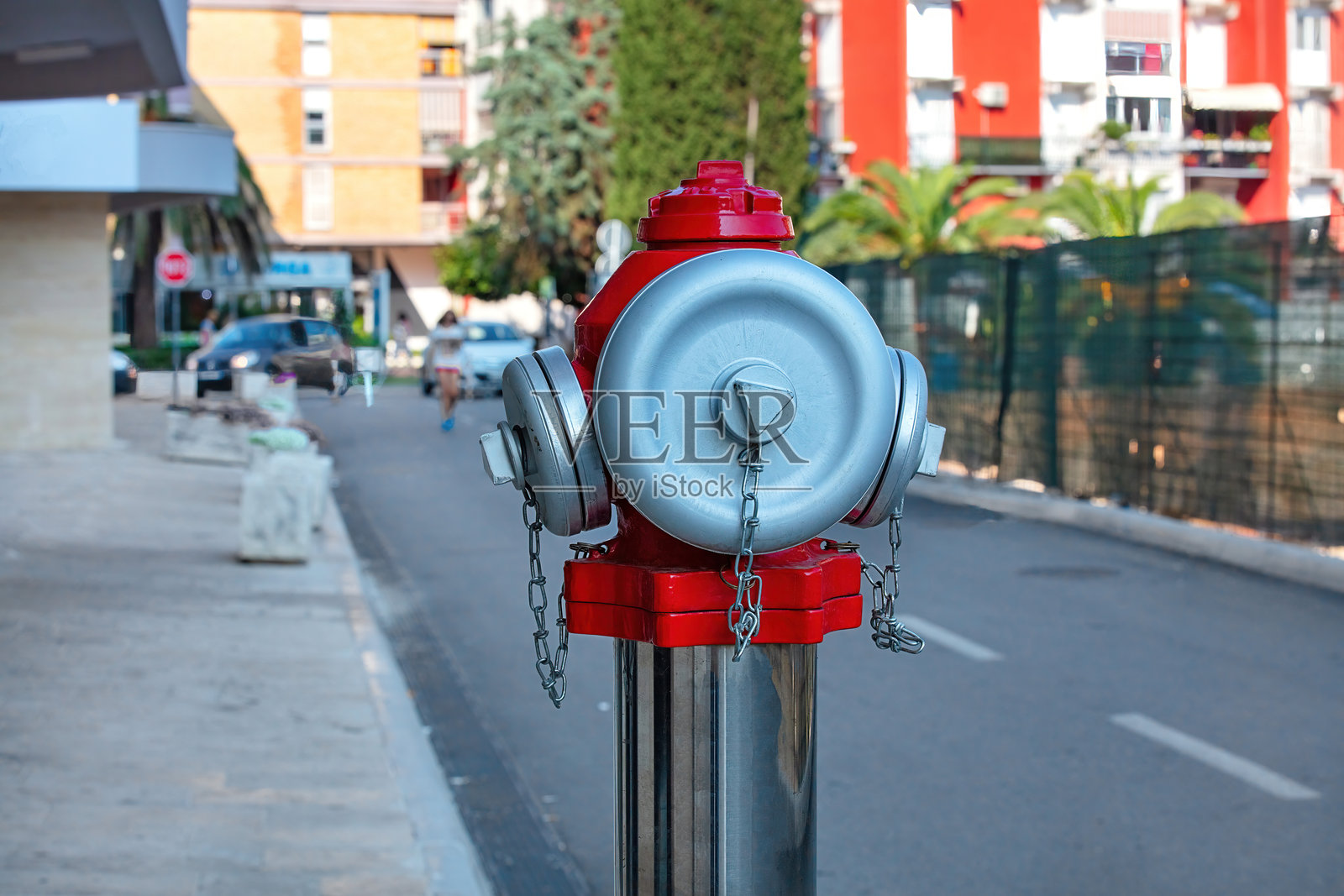 鲜艳的红色消防栓在阳光明媚的城市街道上格外显眼，周围环绕着绿树。照片摄影图片