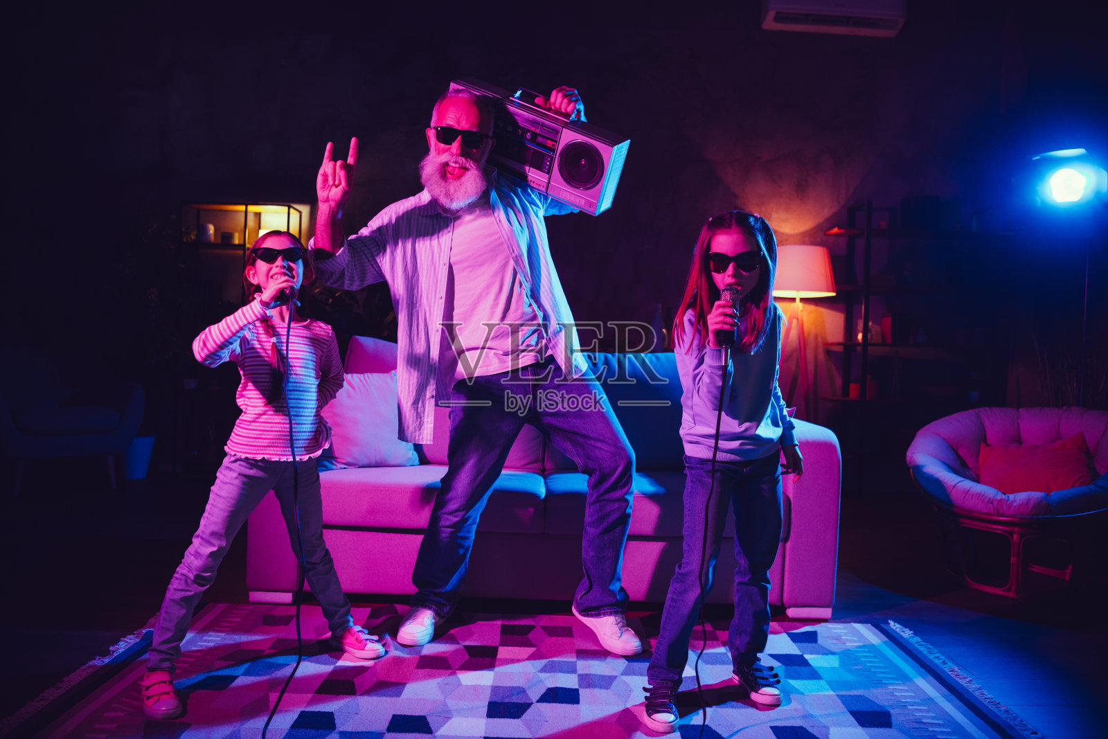 快乐的家庭在家中团聚，一位愉快的老人与两个女孩在晚会庆祝中一起享受卡拉OK。照片摄影图片