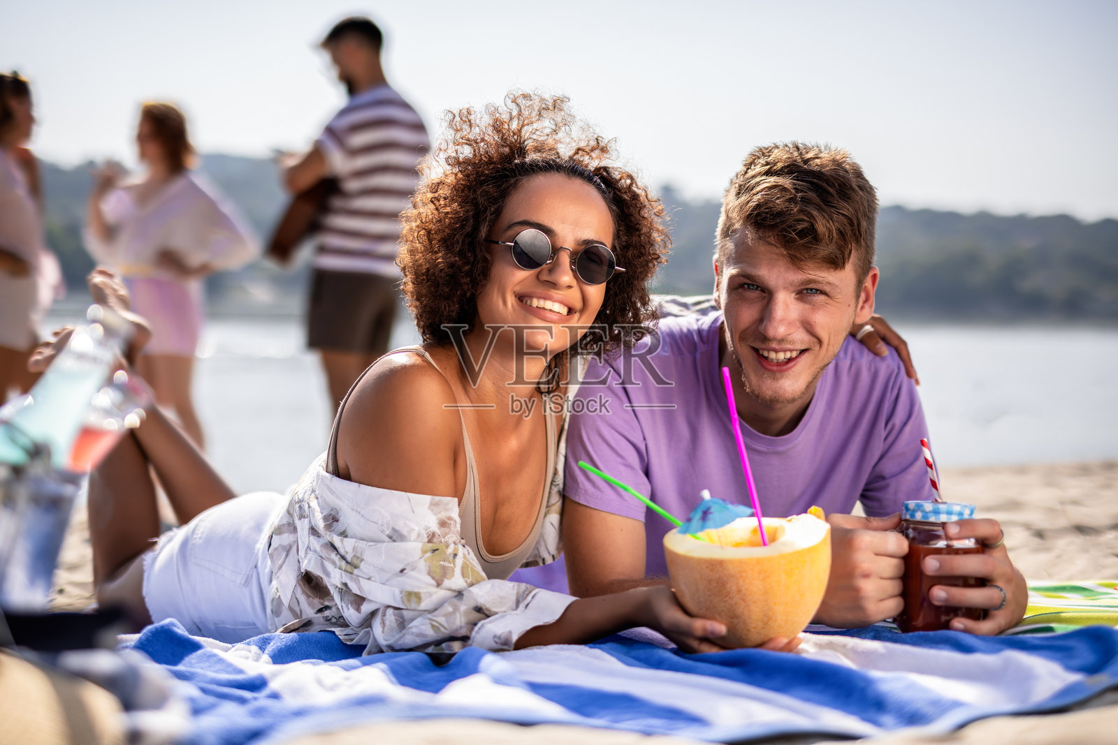 多种族朋友在海滩上野餐，喝椰子水和鸡尾酒。照片摄影图片