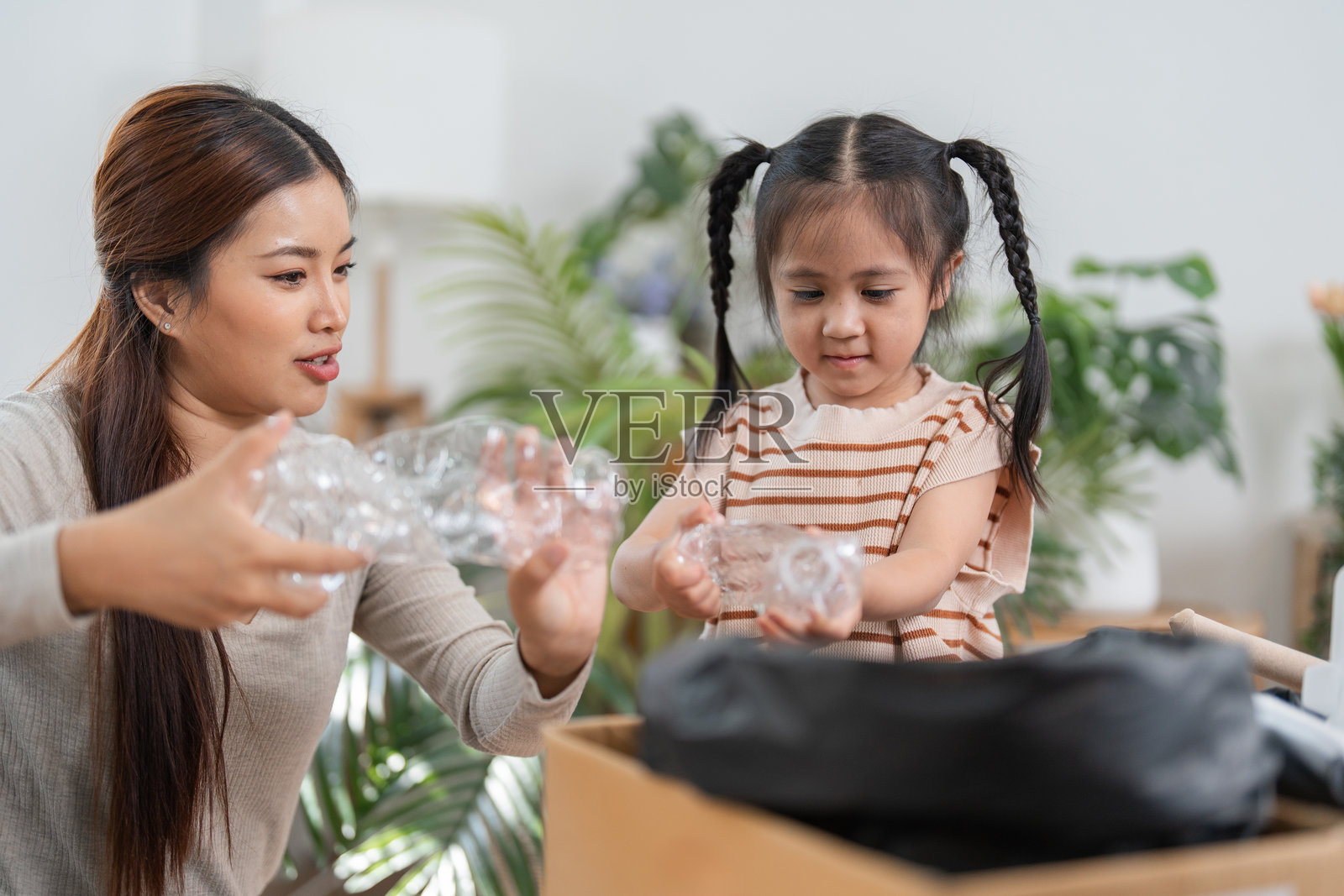 可持续生活与家庭教育。一位母亲在温馨的家中教导女儿关于回收利用及其重要性。照片摄影图片