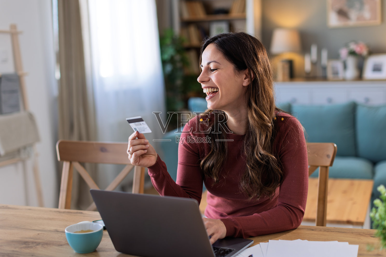 年轻女性坐在沙发上使用笔记本电脑和信用卡进行网上购物和订购照片摄影图片