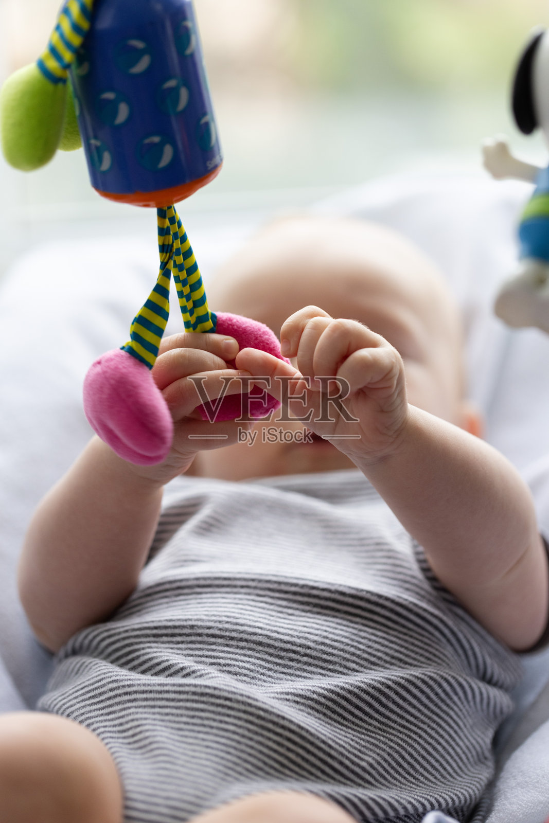 新生儿躺在婴儿椅上，好奇地玩着悬挂的玩具。特写，选择性对焦。照片摄影图片