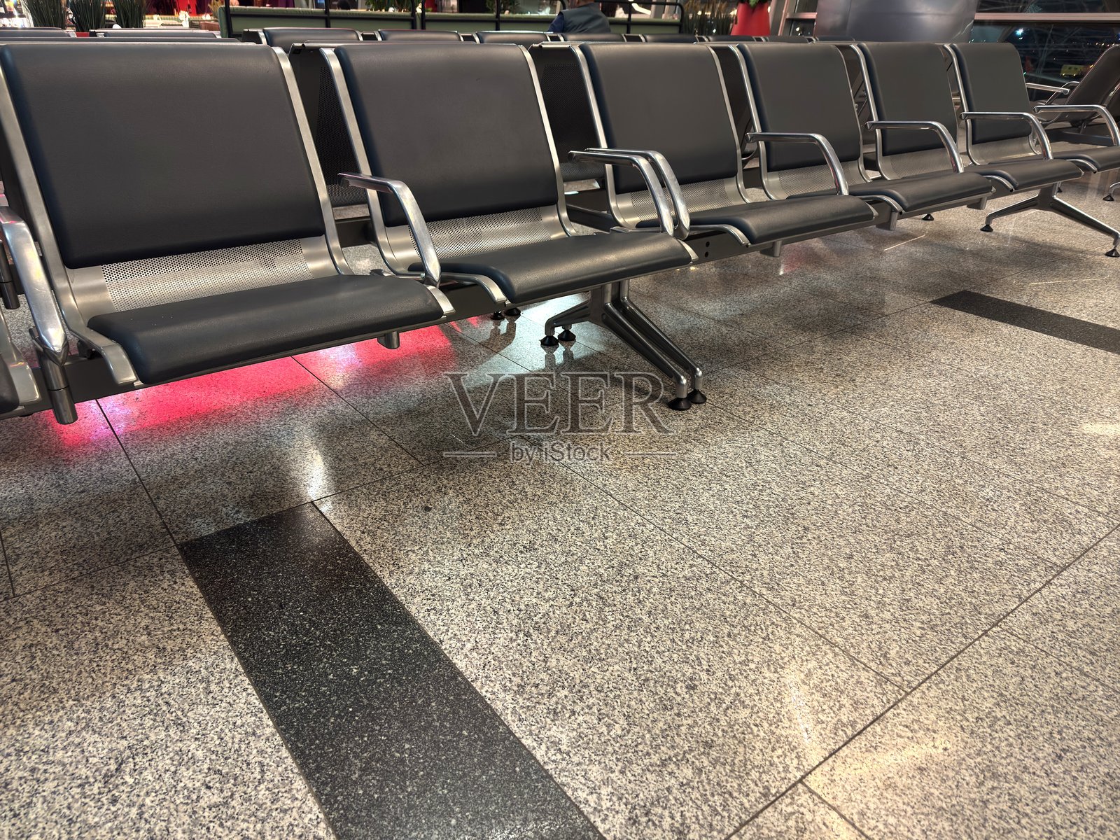 机场的座椅是蓝色的，空荡荡的，配有银色扶手和红色灯光。照片摄影图片