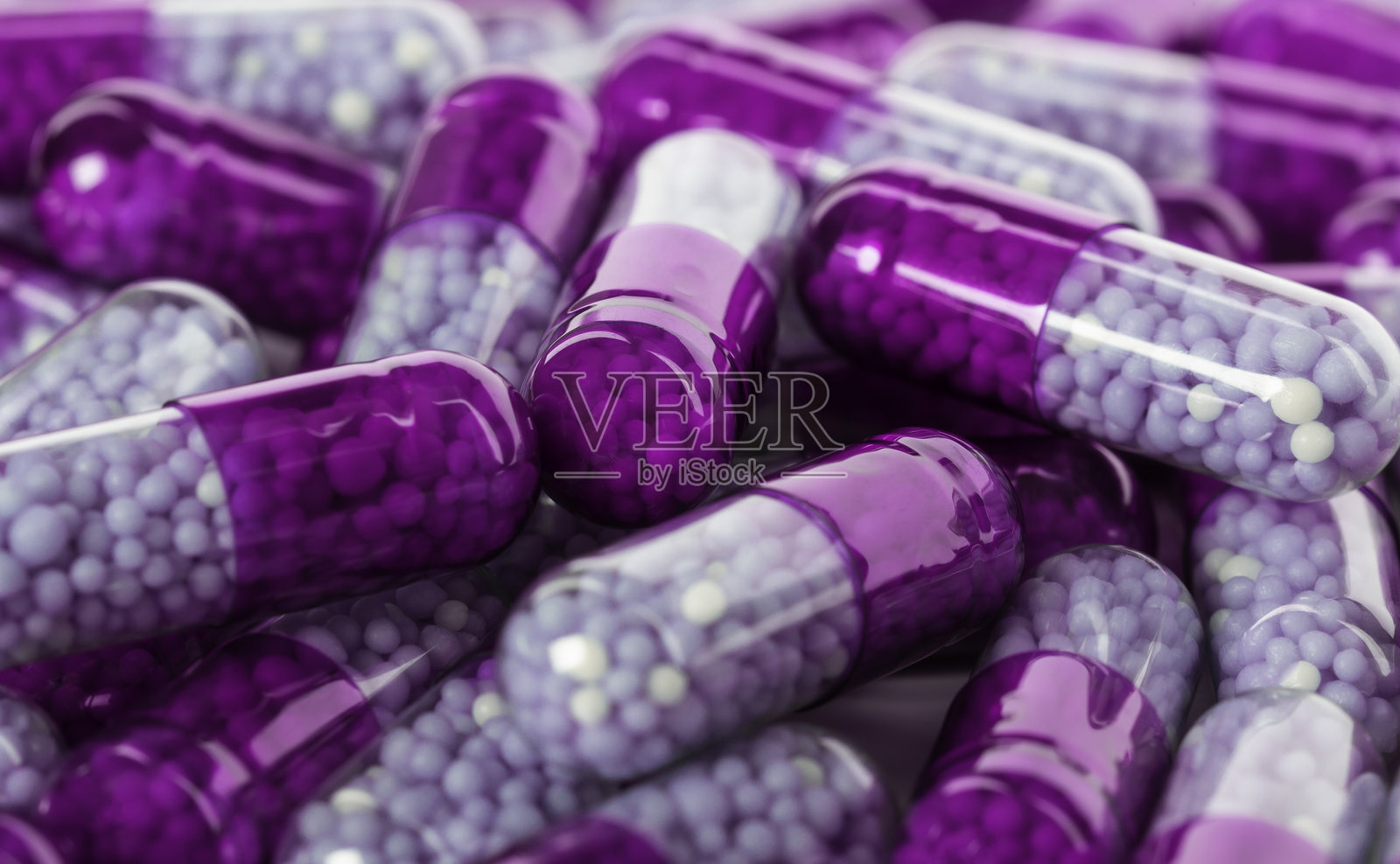 五颜六色的胶囊，紫色外壳和白色颗粒散落在表面，形成了一个生动、引人注目的展示，展现了药品的美丽。照片摄影图片