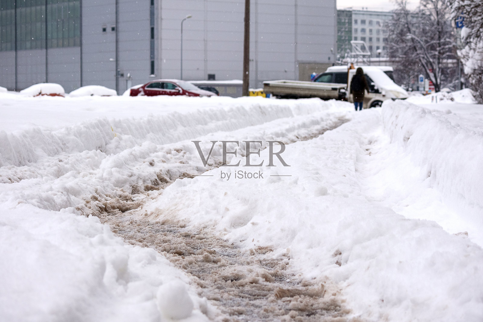 一条有车辙的雪-covered街道，背景中有一个人在清理积雪。照片摄影图片