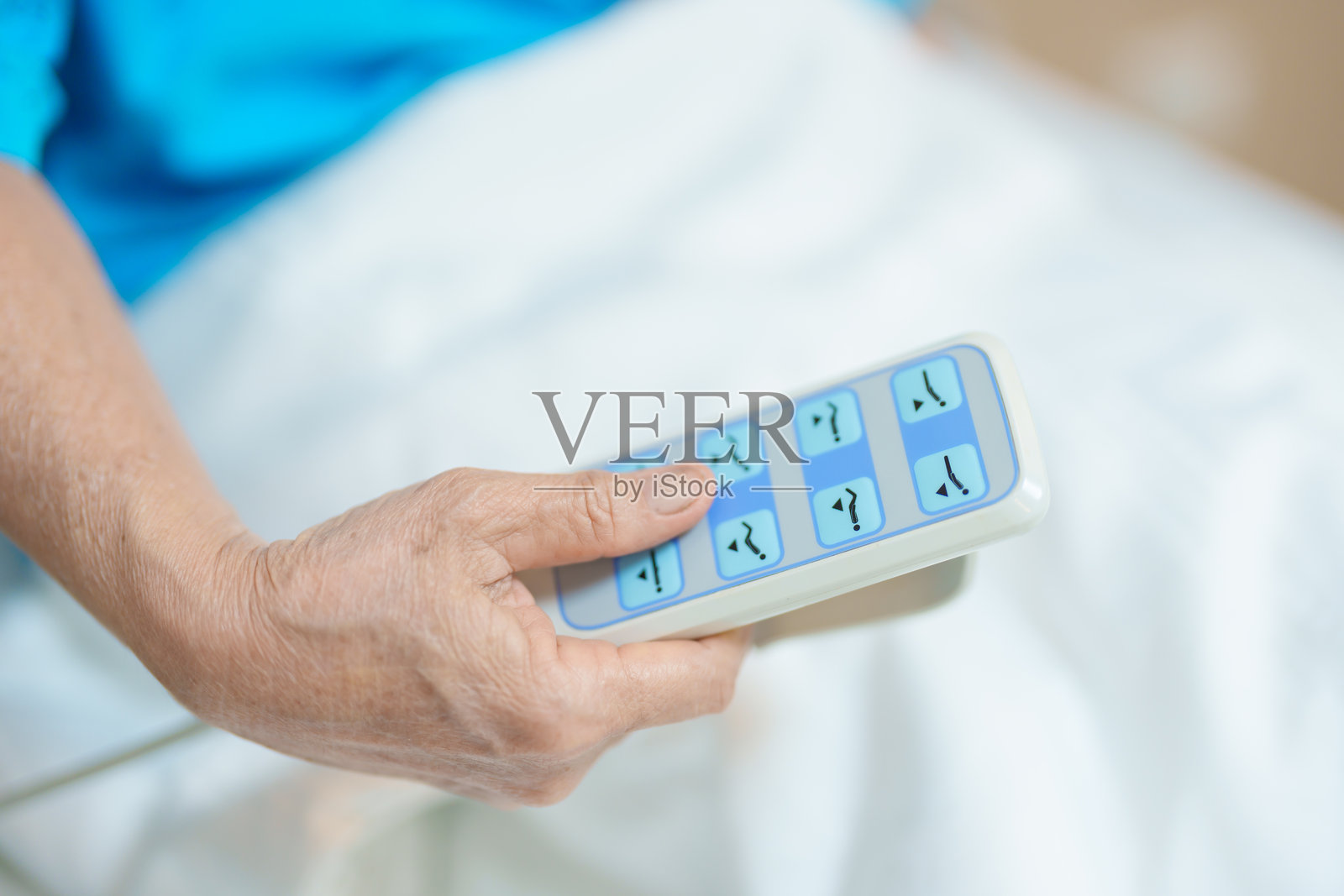 老年亚洲女性患者用遥控器调整医院病房的床位。快乐的老年病人在现代医院的舒适电动床上休息。照片摄影图片