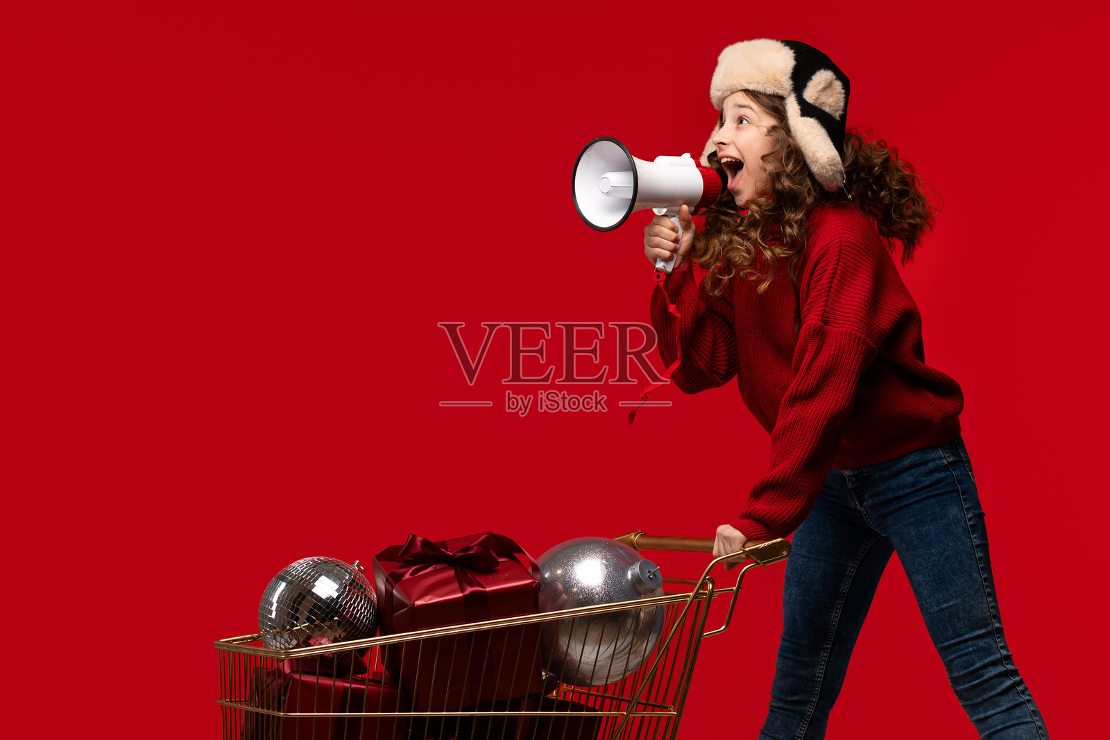 穿着毛衣和毛皮帽的活力女孩对着扩音器大喊照片摄影图片