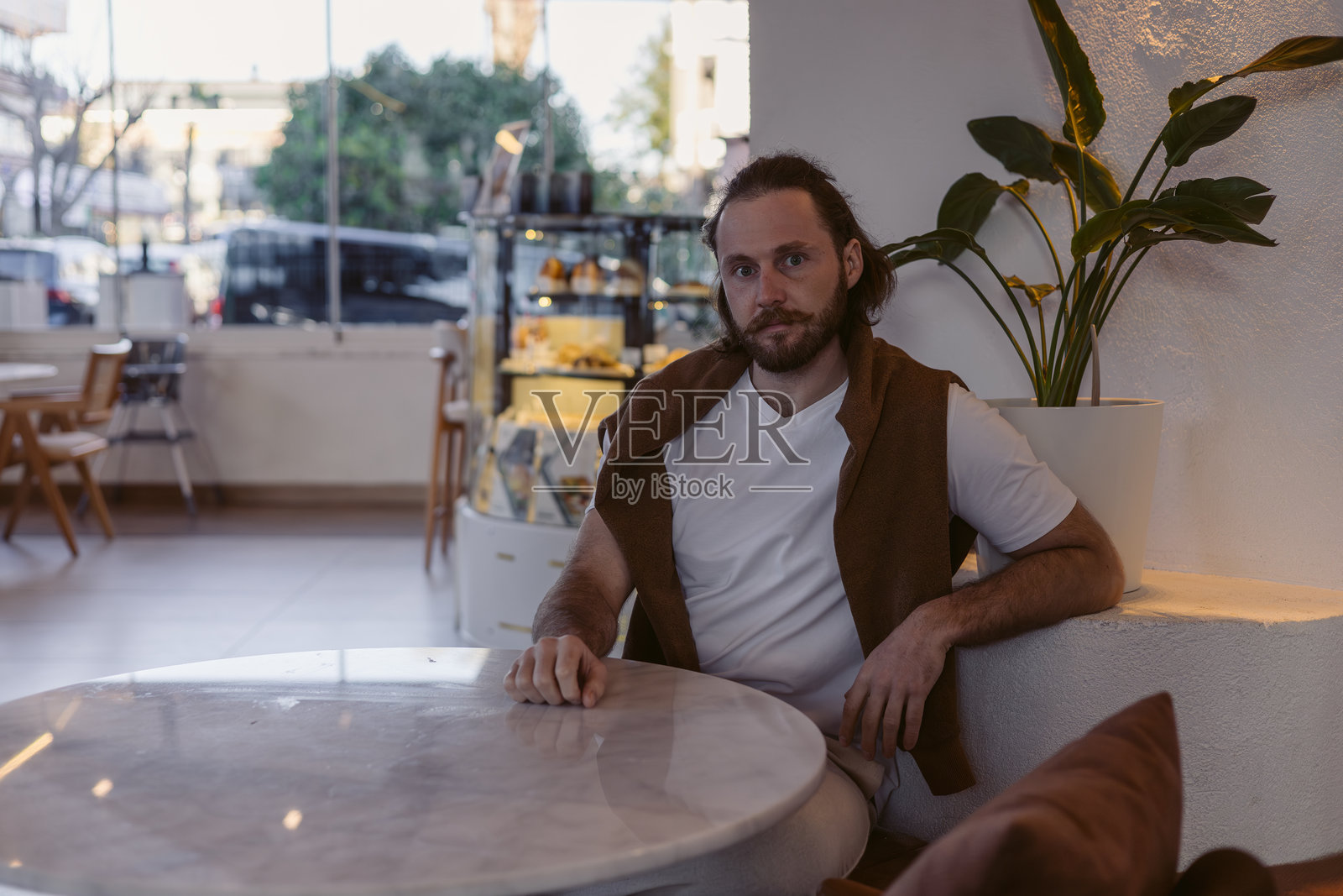 男子在现代咖啡馆的玛瑙桌旁坐着，正值下午晚些时候。照片摄影图片