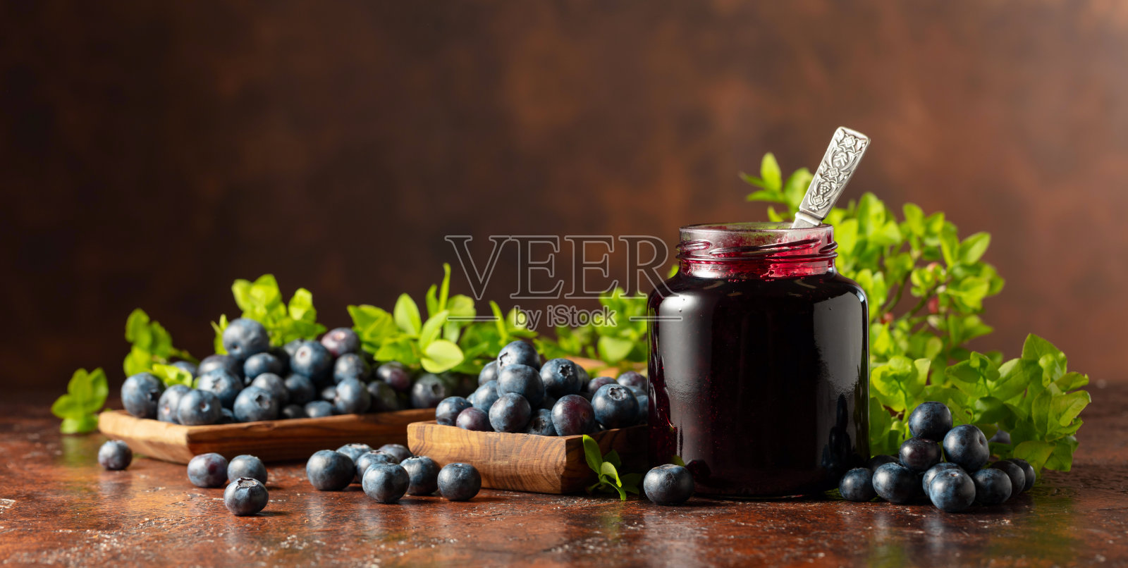 蓝莓果酱和新鲜浆果在棕色背景上。照片摄影图片