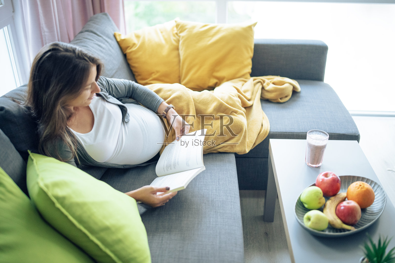 中年孕妇在家沙发上放松并阅读一本书。照片摄影图片