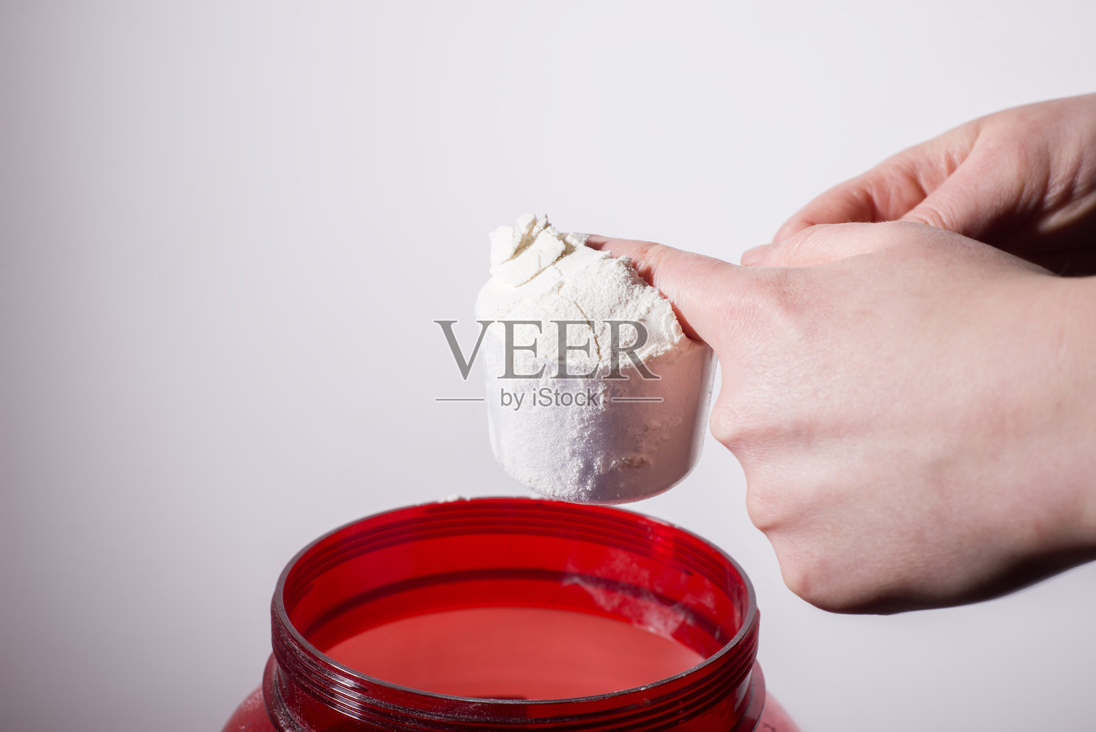 用勺子从红色罐子中测量专业蛋白质的手指，背景为白色照片摄影图片