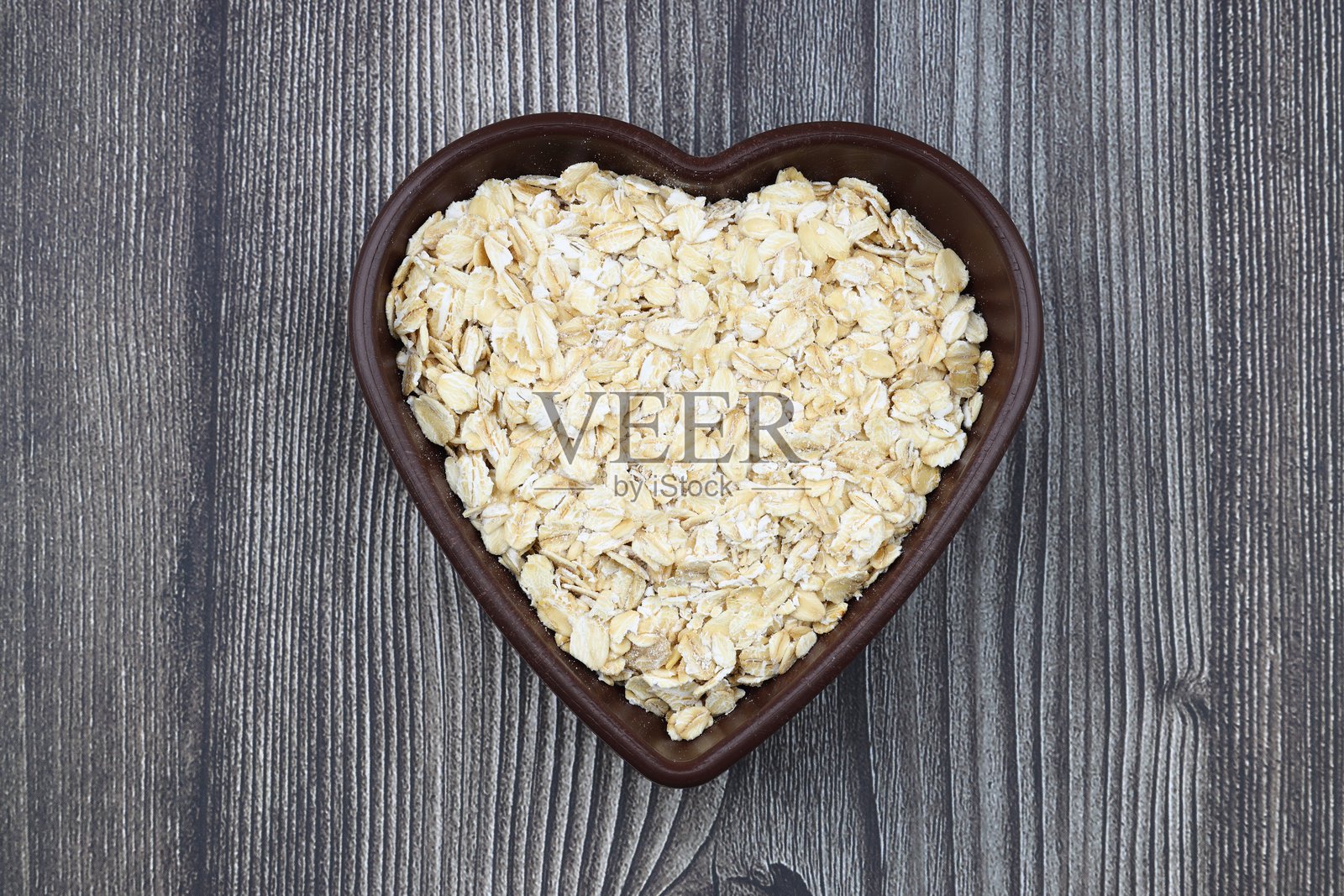 心形盘子上的燕麦片和燕麦，背景为黑色。健康早餐。有机素食。照片摄影图片