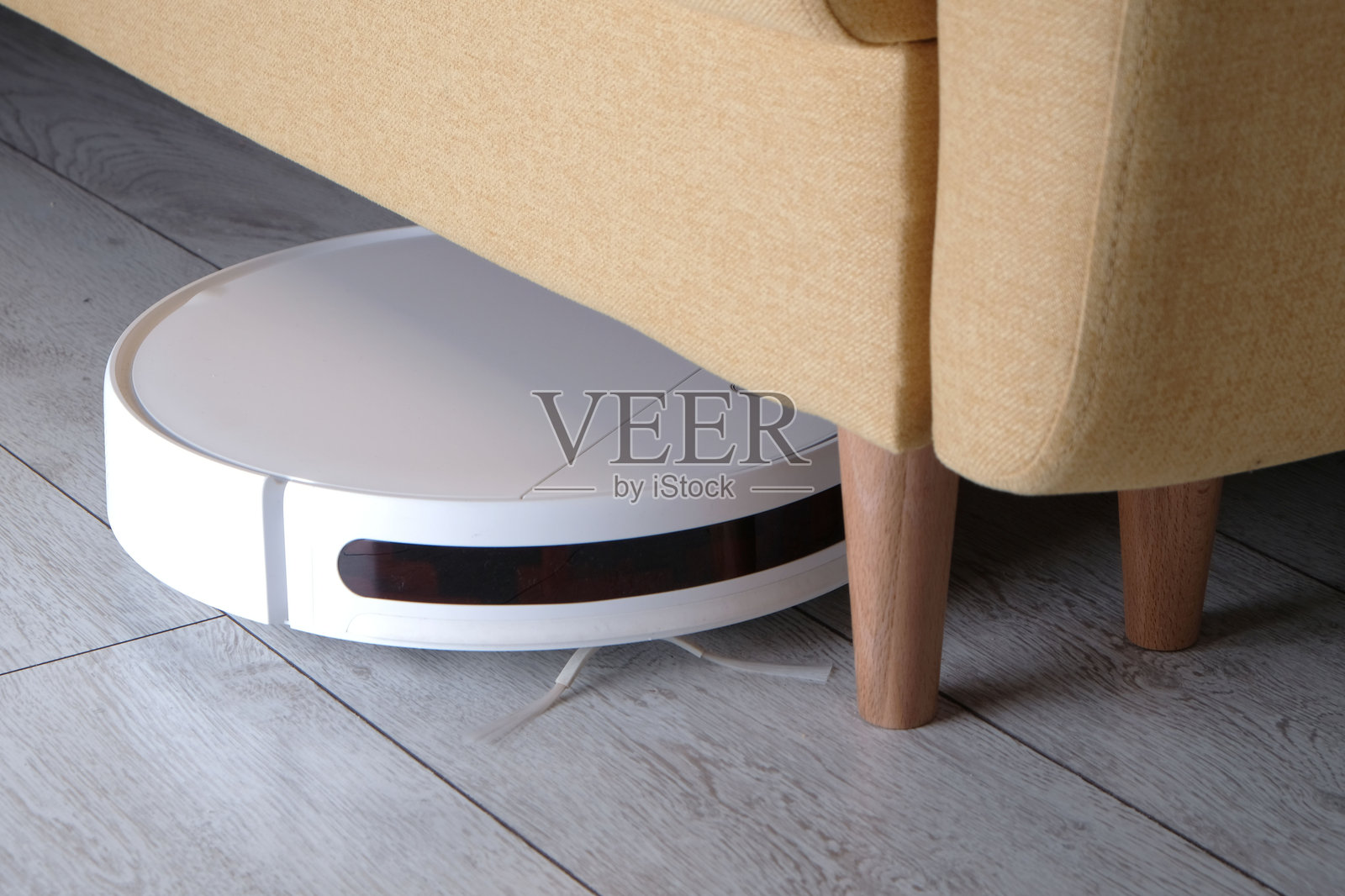 白色机器人吸尘器在沙发下清除灰尘，智能家居电器照片摄影图片