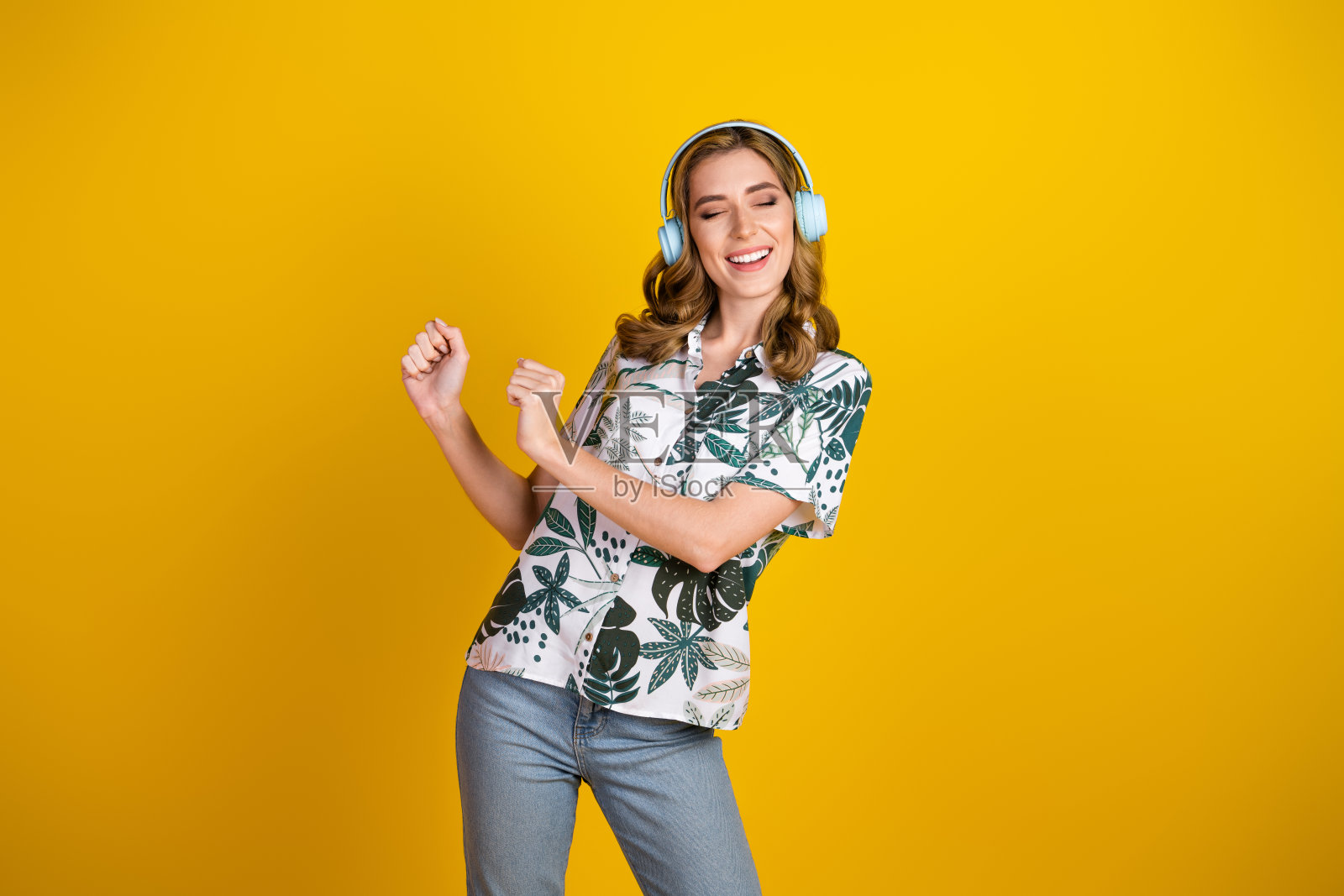 快乐的年轻女性戴着耳机在音乐中跳舞，展现出幸福和乐趣，背景是鲜艳的黄色。照片摄影图片