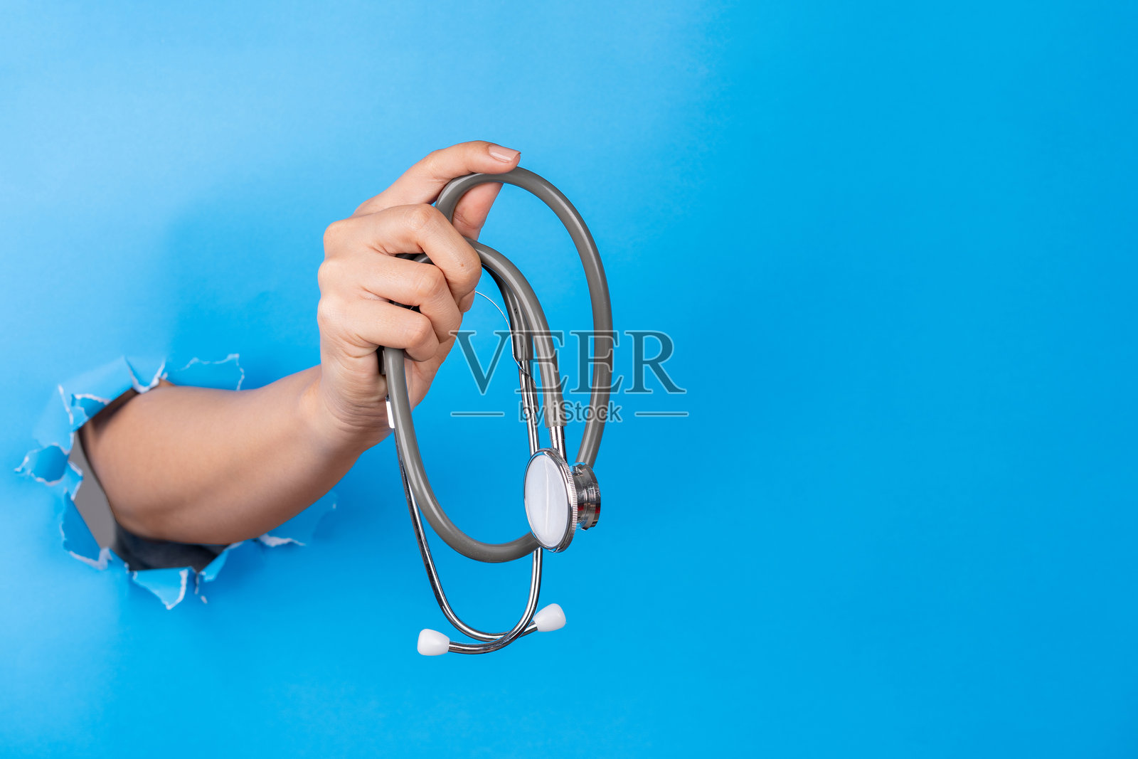 手握听诊器穿过蓝色纸张的孔照片摄影图片