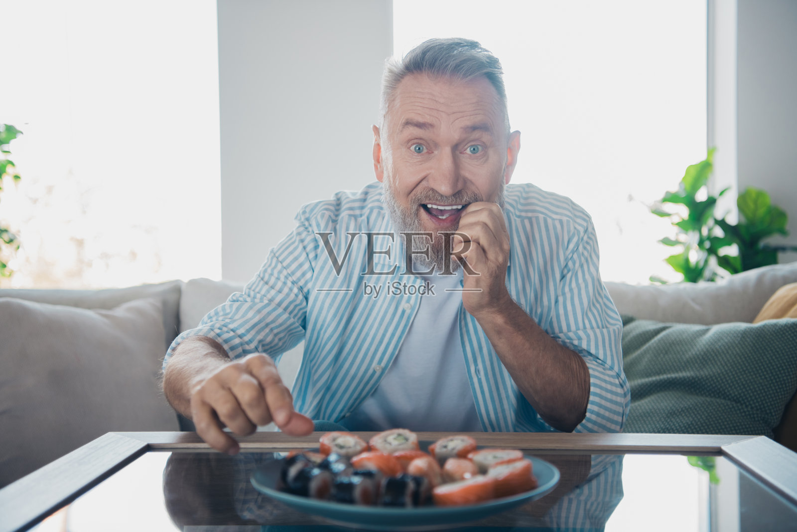 穿着条纹衬衫的老人微笑着，在明亮舒适的室内客厅中放松度过轻松的一天照片摄影图片