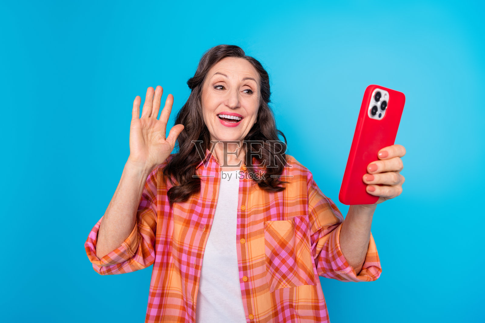 微笑的女性在蓝色背景下做手势，手持智能手机，穿着鲜艳的格子衬衫照片摄影图片
