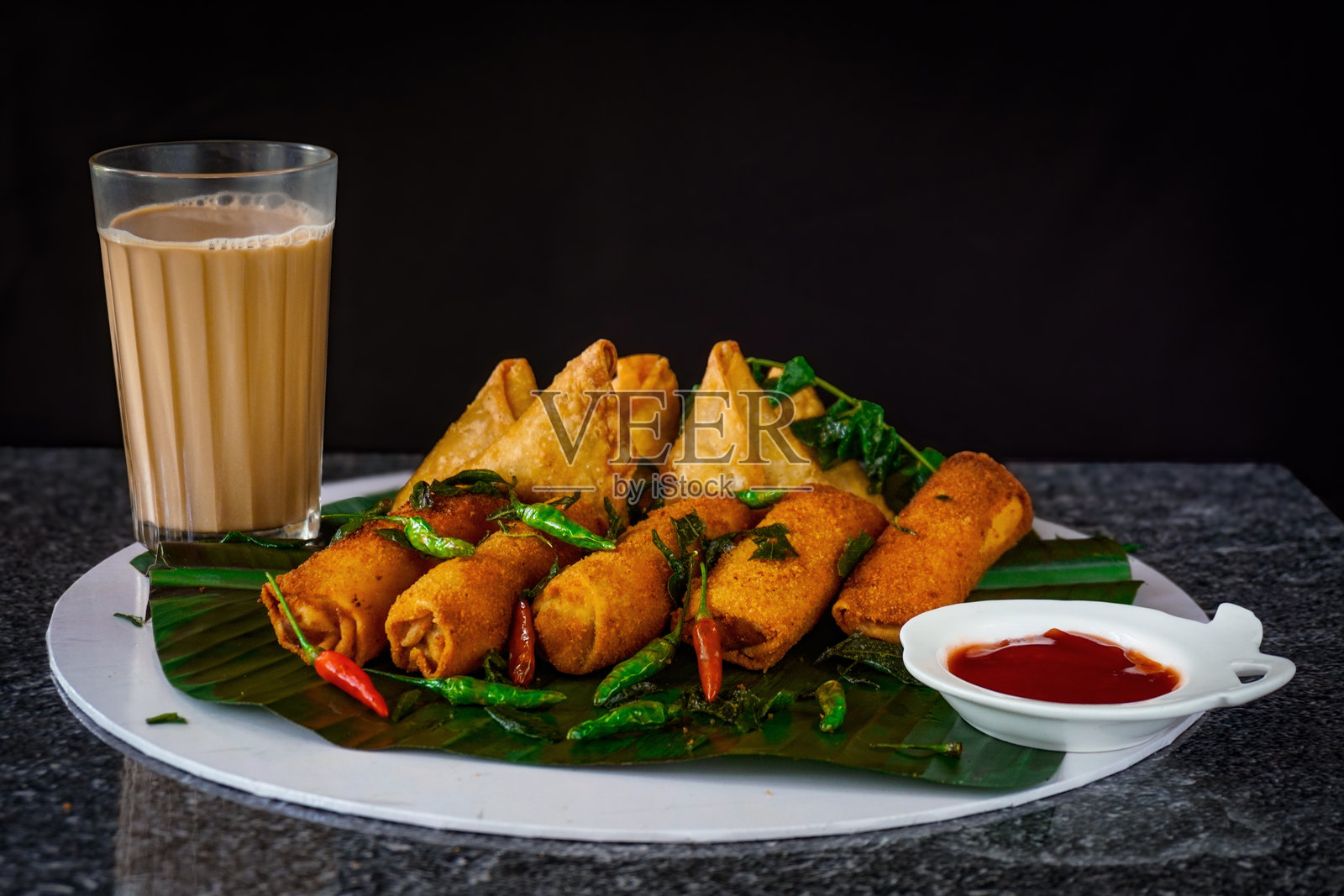 斯里兰卡快餐托盘 / 在香蕉叶上盛放的蛋卷和萨莫萨，配有奶茶、番茄酱、凯特酱和新鲜咖喱叶照片摄影图片