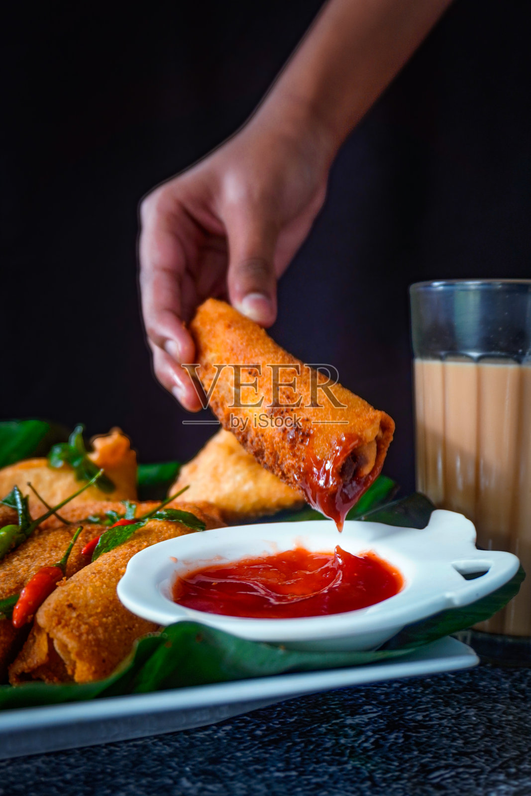 斯里兰卡美食特写 / 手将萨莫萨和蛋卷浸入番茄酱，配有奶茶、辣椒和咖喱叶照片摄影图片