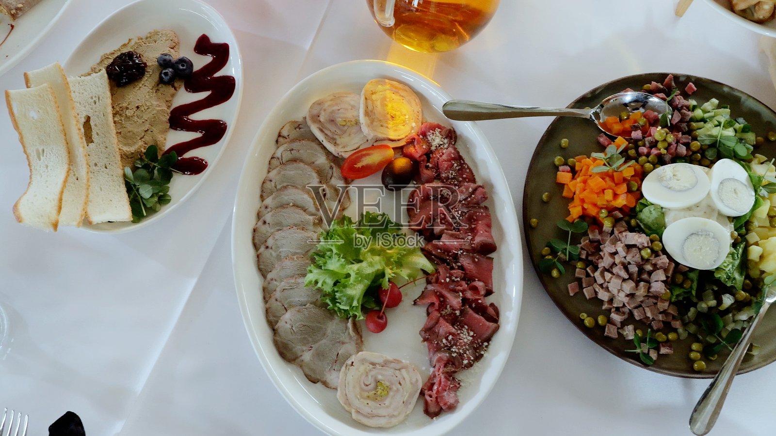 精致的肉类拼盘，包含切片肉类、奶油肝酱、烤面包和新鲜沙拉，艺术地摆放在洁白的亚麻布上。照片摄影图片