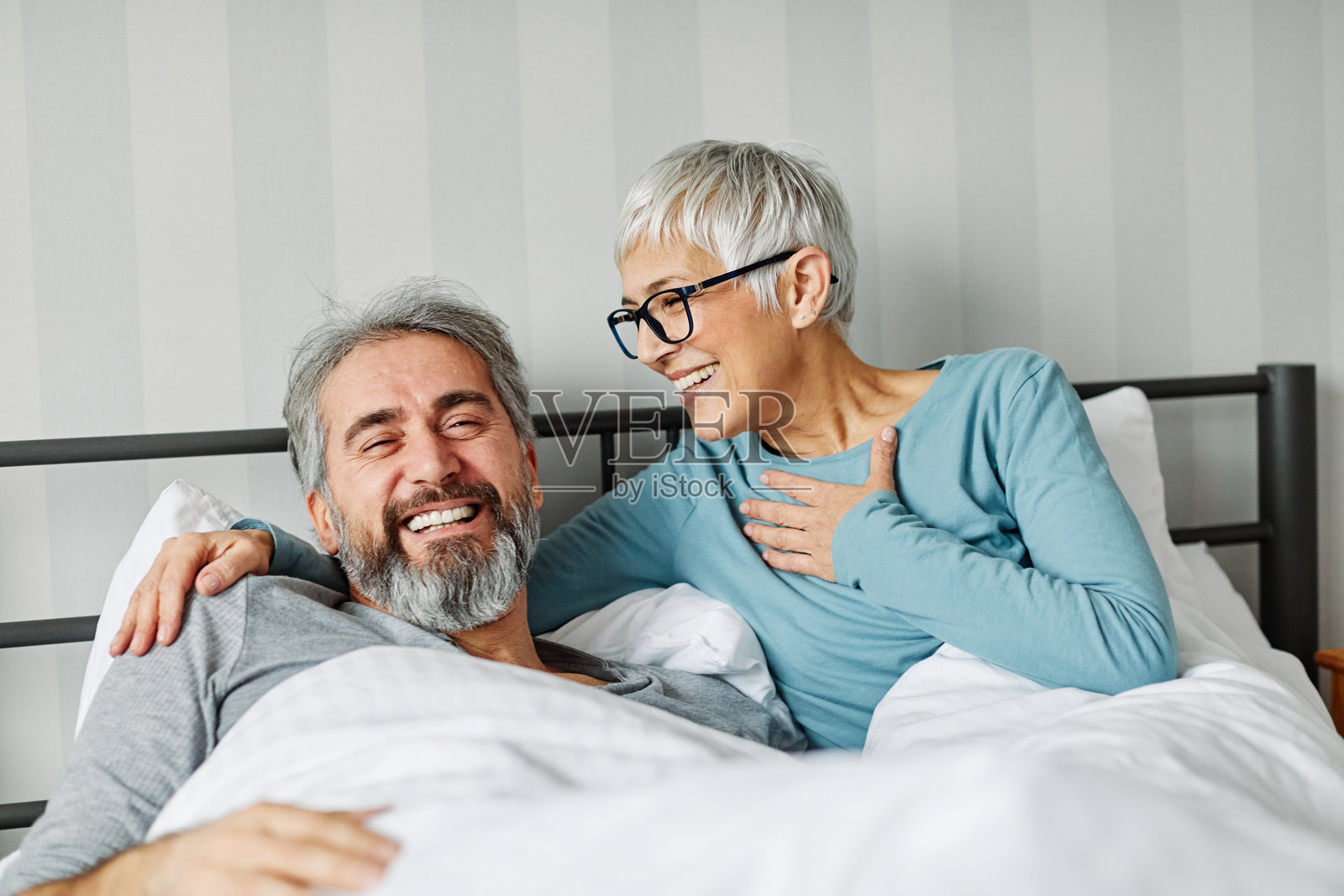快乐的退休老年夫妇在卧室里相拥而卧，享受轻松的时光。照片摄影图片