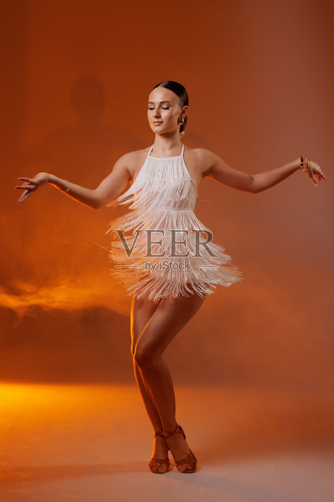 优雅的拉丁女舞者身穿白色流苏裙，在艺术灯光下自信而优雅地表演动态舞姿。照片摄影图片