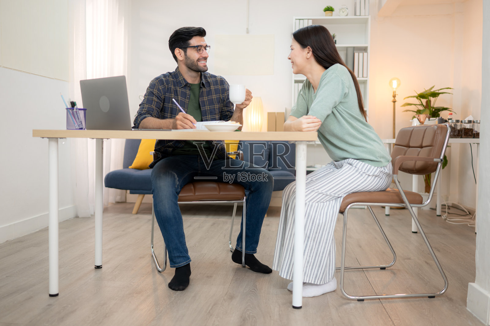 年轻自由职业者在家与女友一起用笔记本电脑在线工作，面带微笑的肖像照片摄影图片