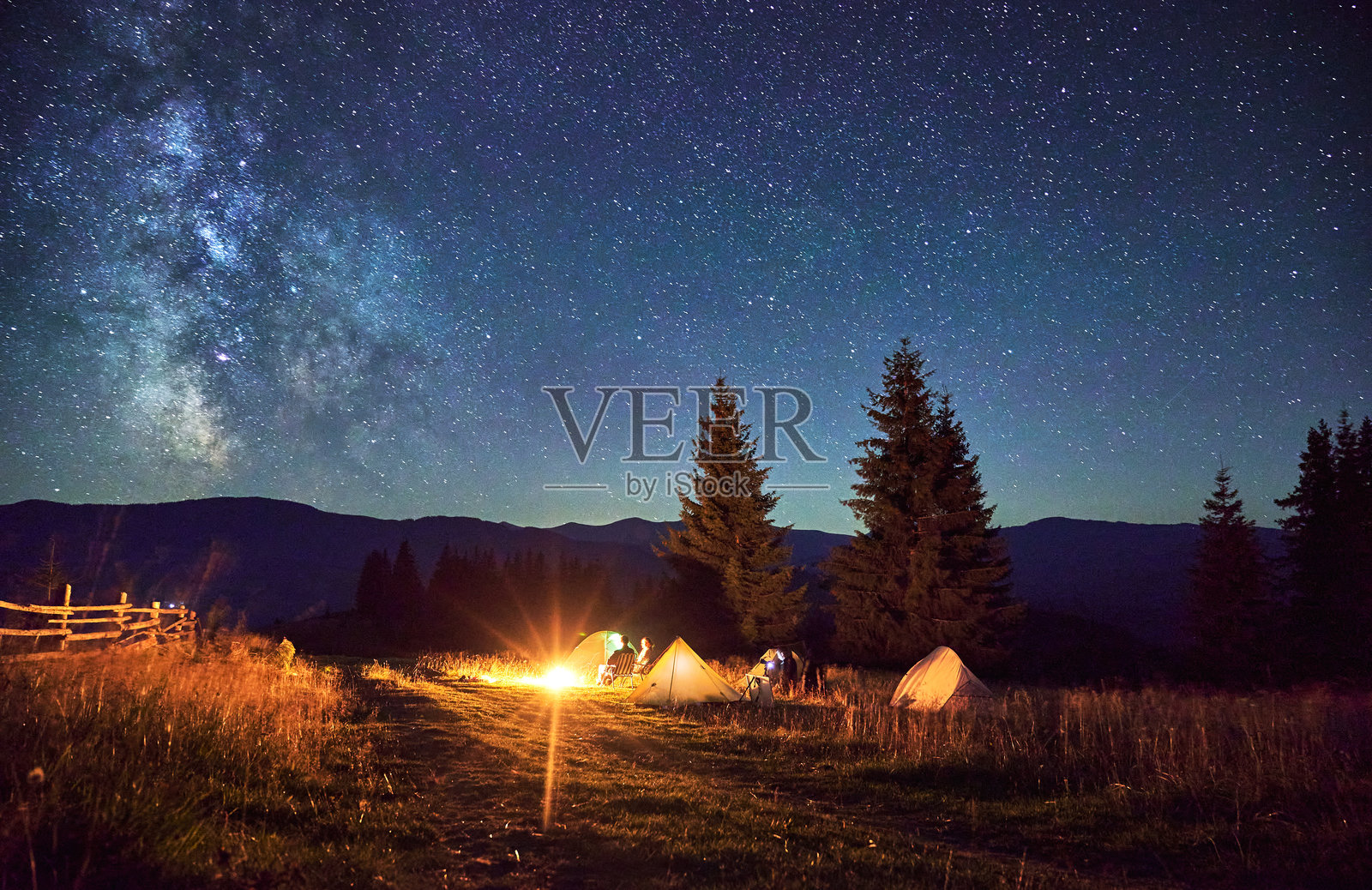 一群徒步旅行者在篝火旁休息，周围是闪烁的帐篷和壮丽的星空。照片摄影图片